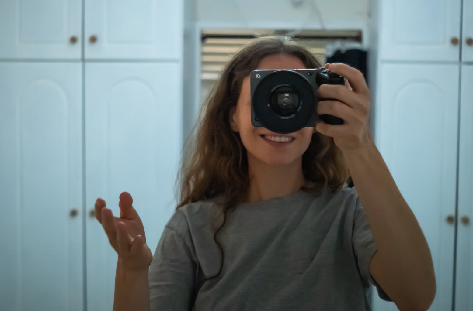 Talya Otzar photographing her own reflection in a mirror, camera raised to her eye