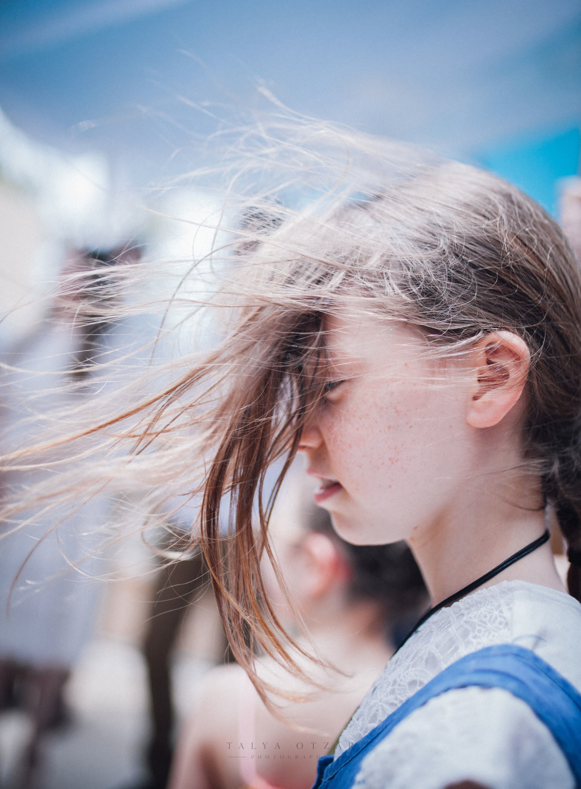 A girl's hair blown across her face in the sea wind on a bright day