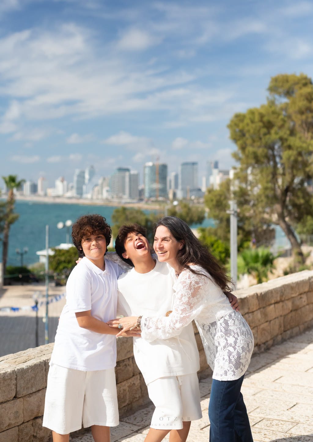 A mother laughing with her two sons above the water, the Tel Aviv skyline across the bay