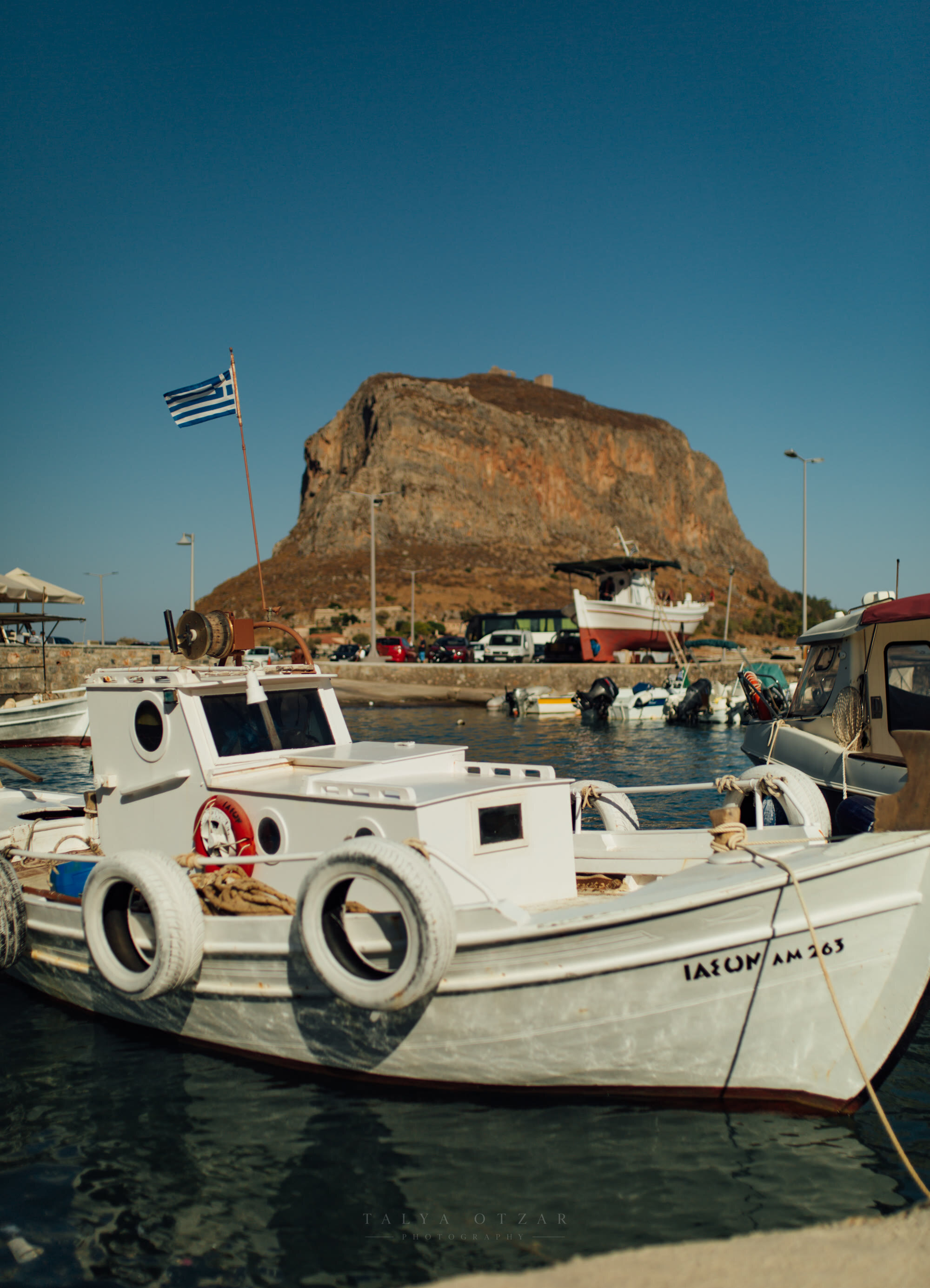 A fishing boat moored below the great rock of Monemvasia, a Greek flag flying above the quay