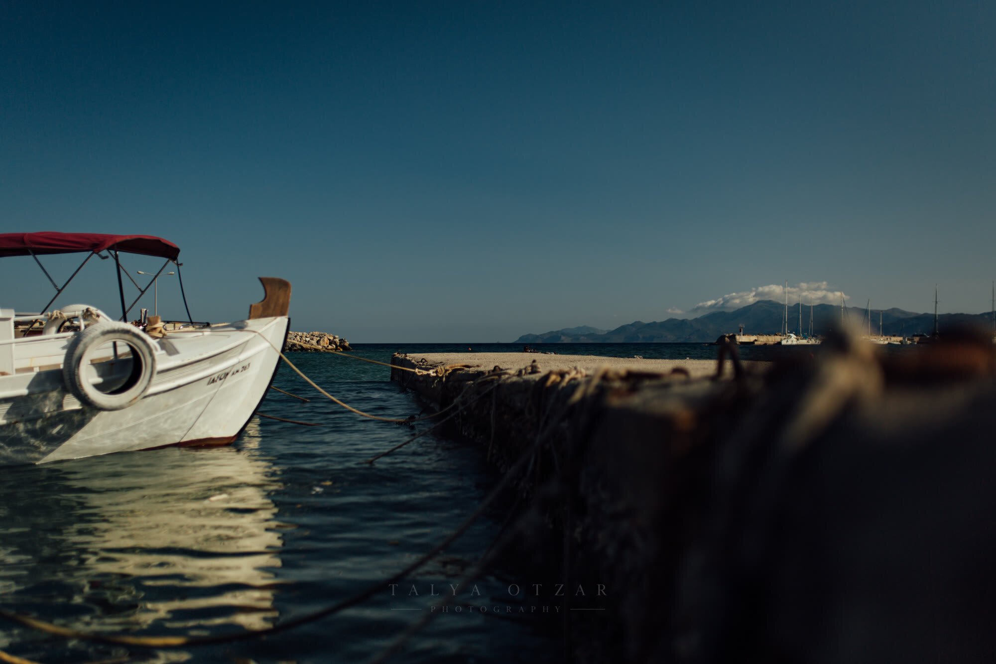 A moored boat and the harbour wall at dusk, mountains rising across the bay