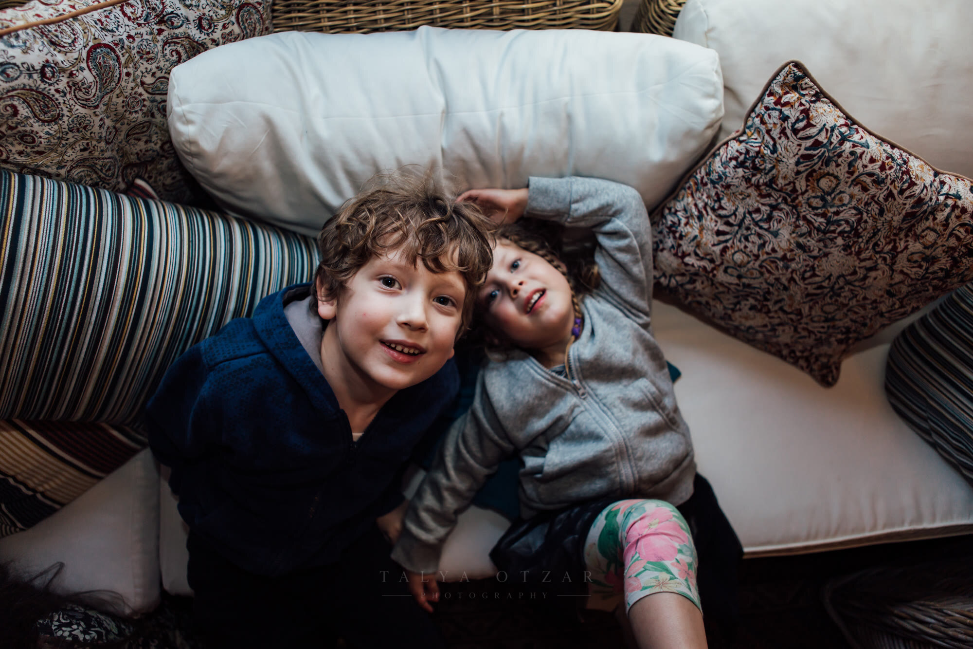 Brother and sister lying head to head on the cushions, looking straight up at the camera