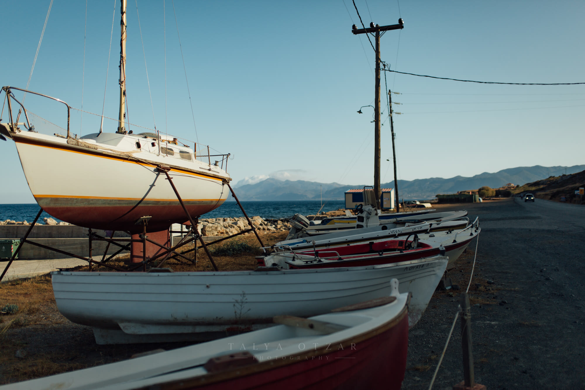 Boats pulled up on the stony shore at sunset, mountains across the water