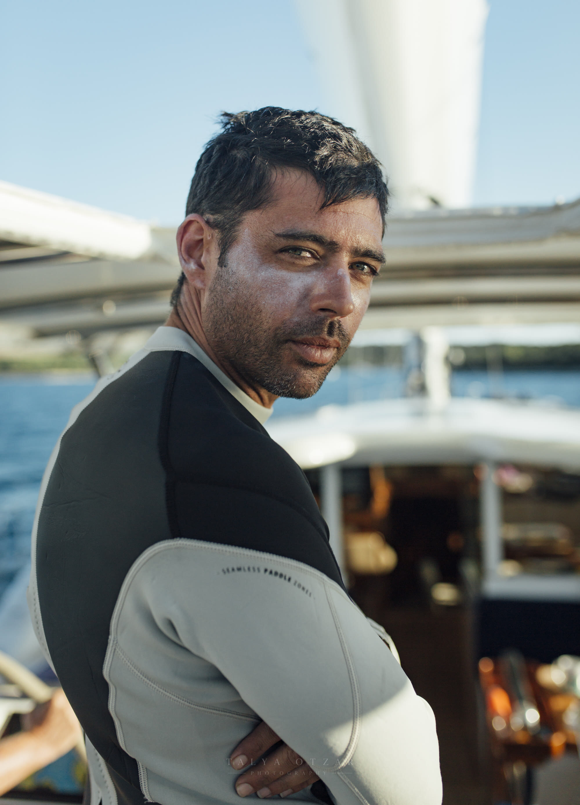 A man in a wetsuit looking back over his shoulder on the deck of a yacht