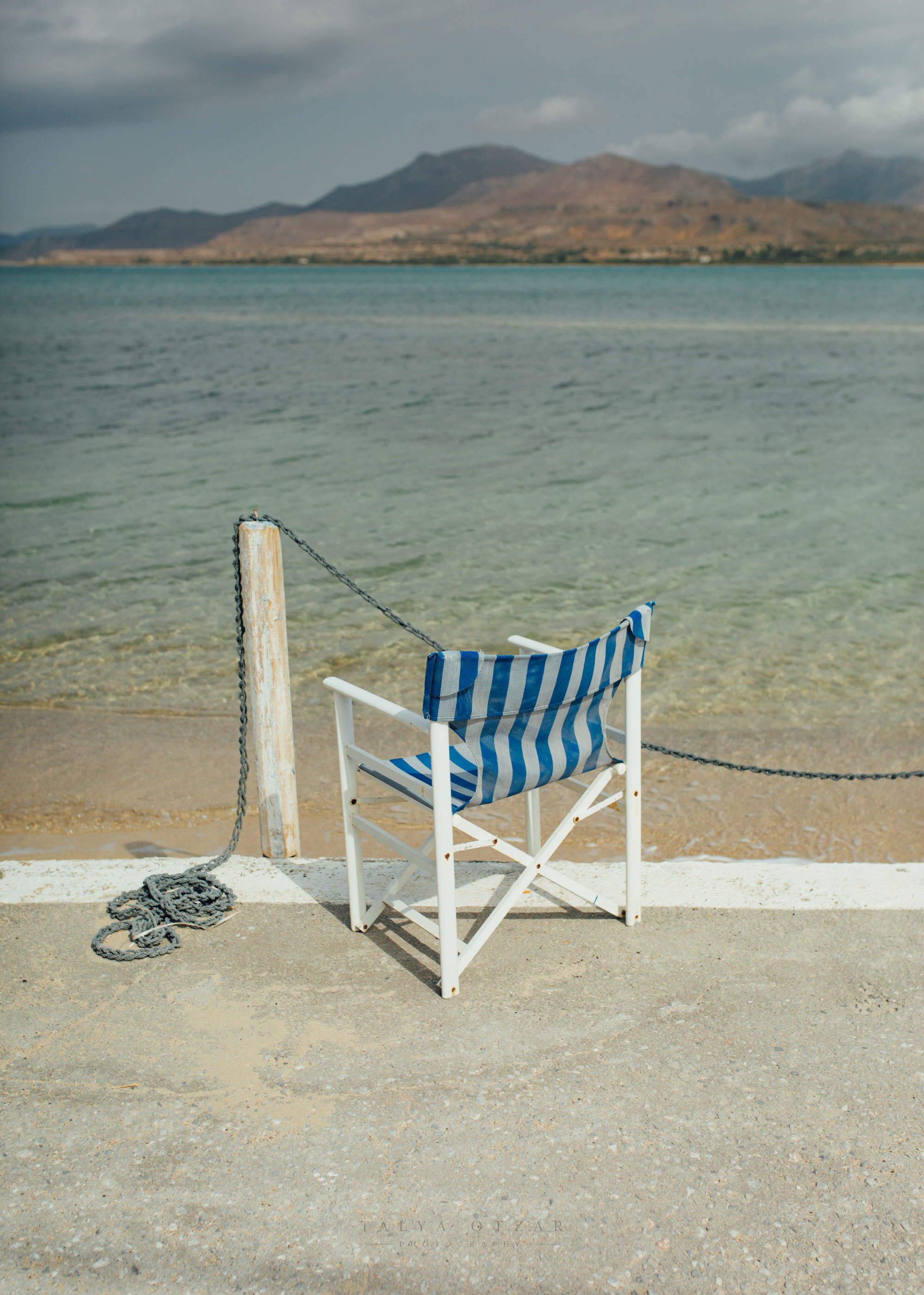 A striped deckchair standing alone at the water's edge under a heavy sky