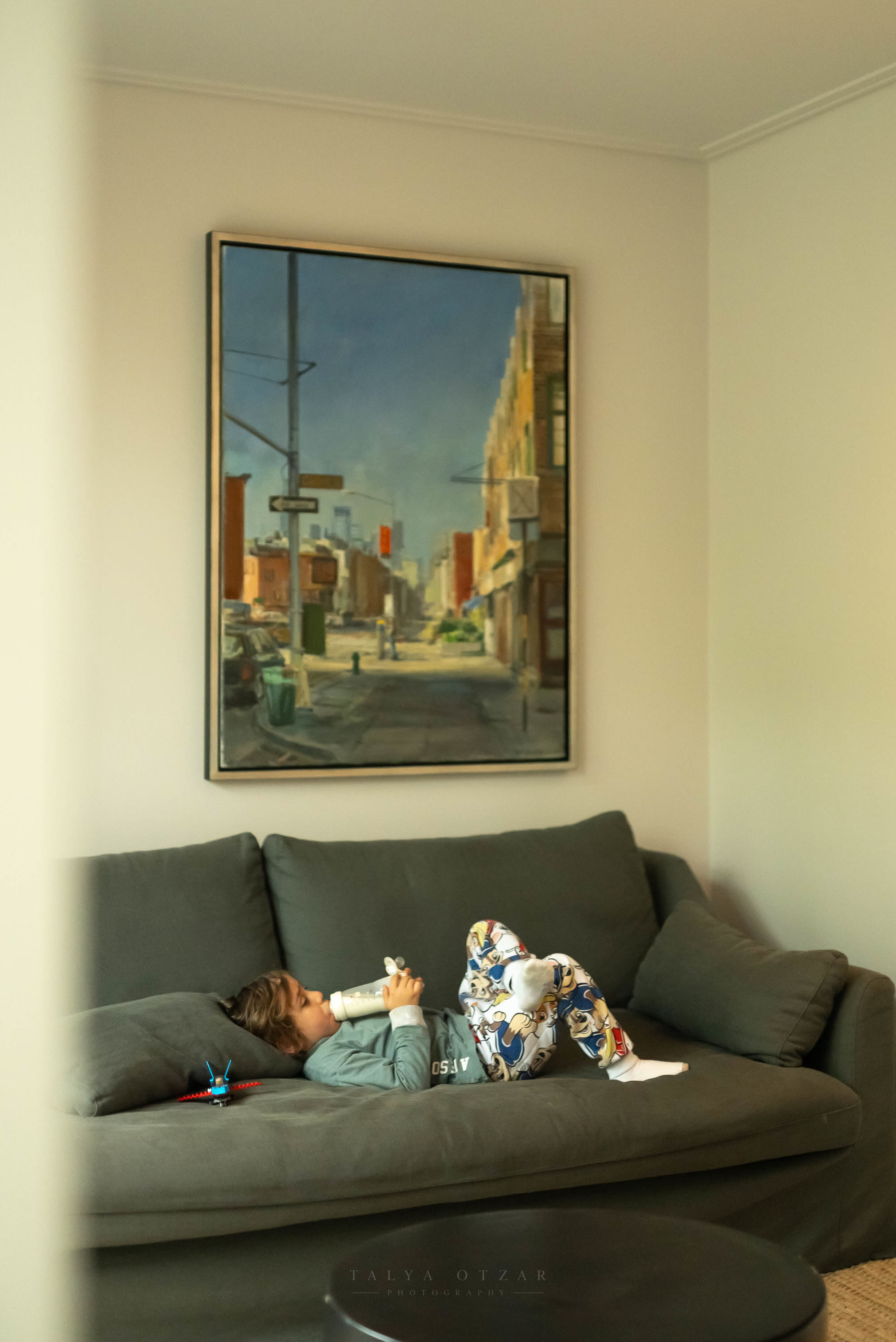 A child lying on the sofa with a bottle beneath a large framed painting