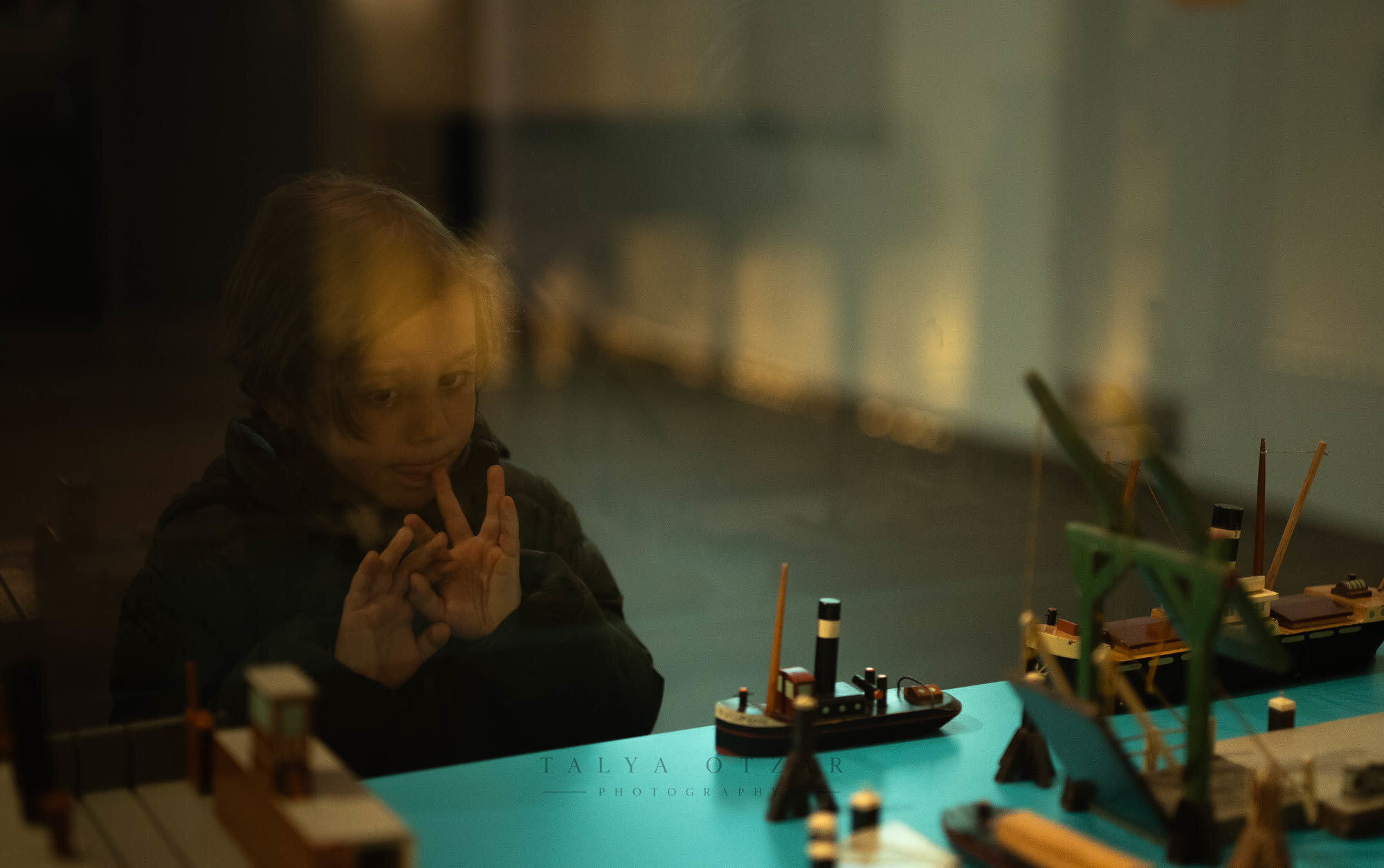 A child reflected in the glass of a museum case of model boats