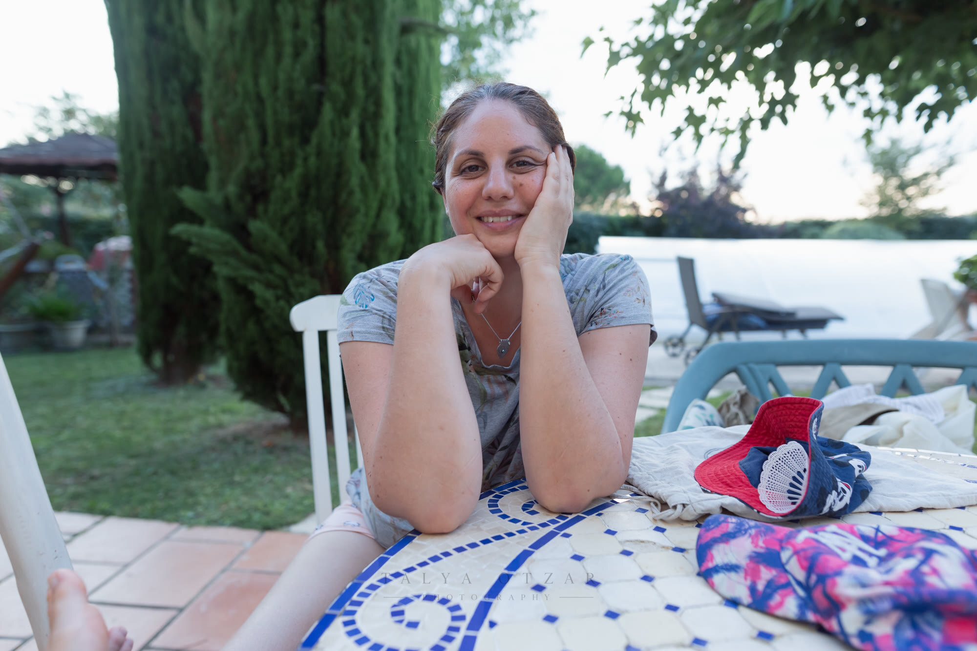 A woman resting her chin on her hands at the mosaic garden table