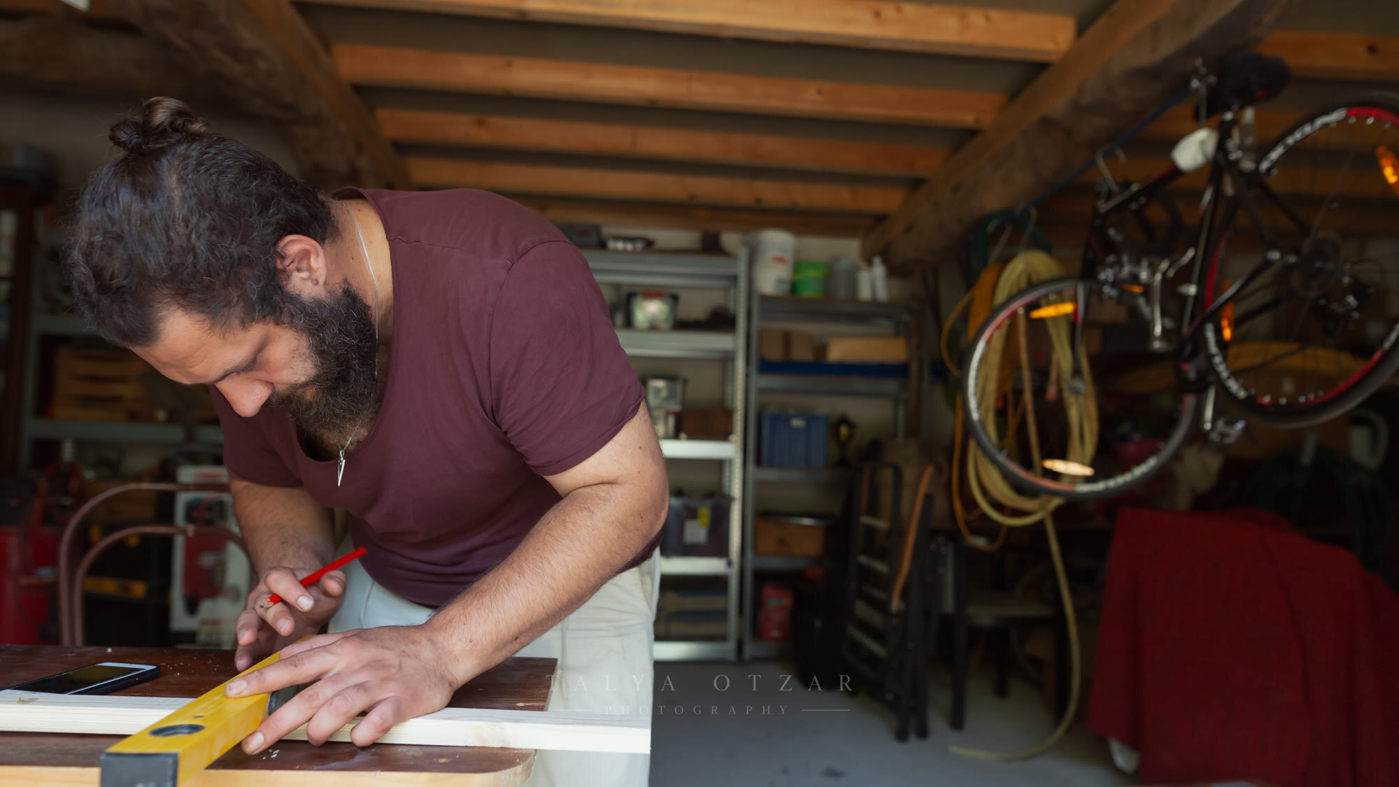 A man measuring and marking a length of timber on the workbench in the garage