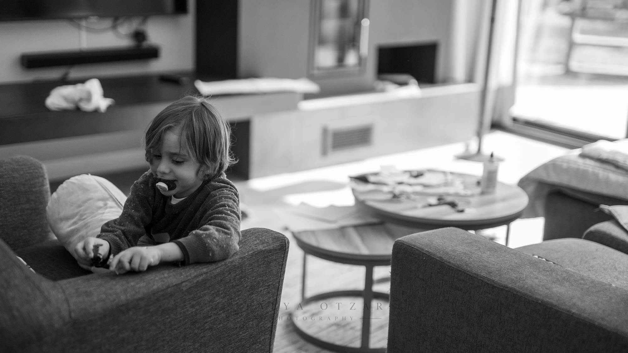 A toddler leaning over the back of an armchair in a bright living room