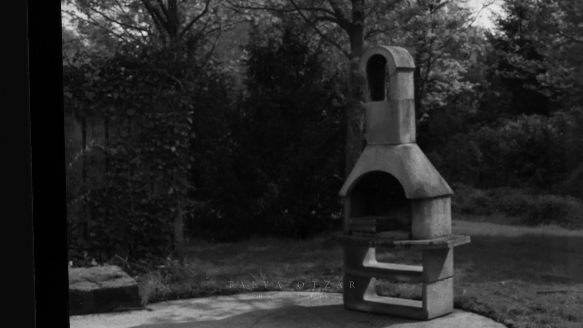 A stone garden barbecue standing in the green, seen through the window frame