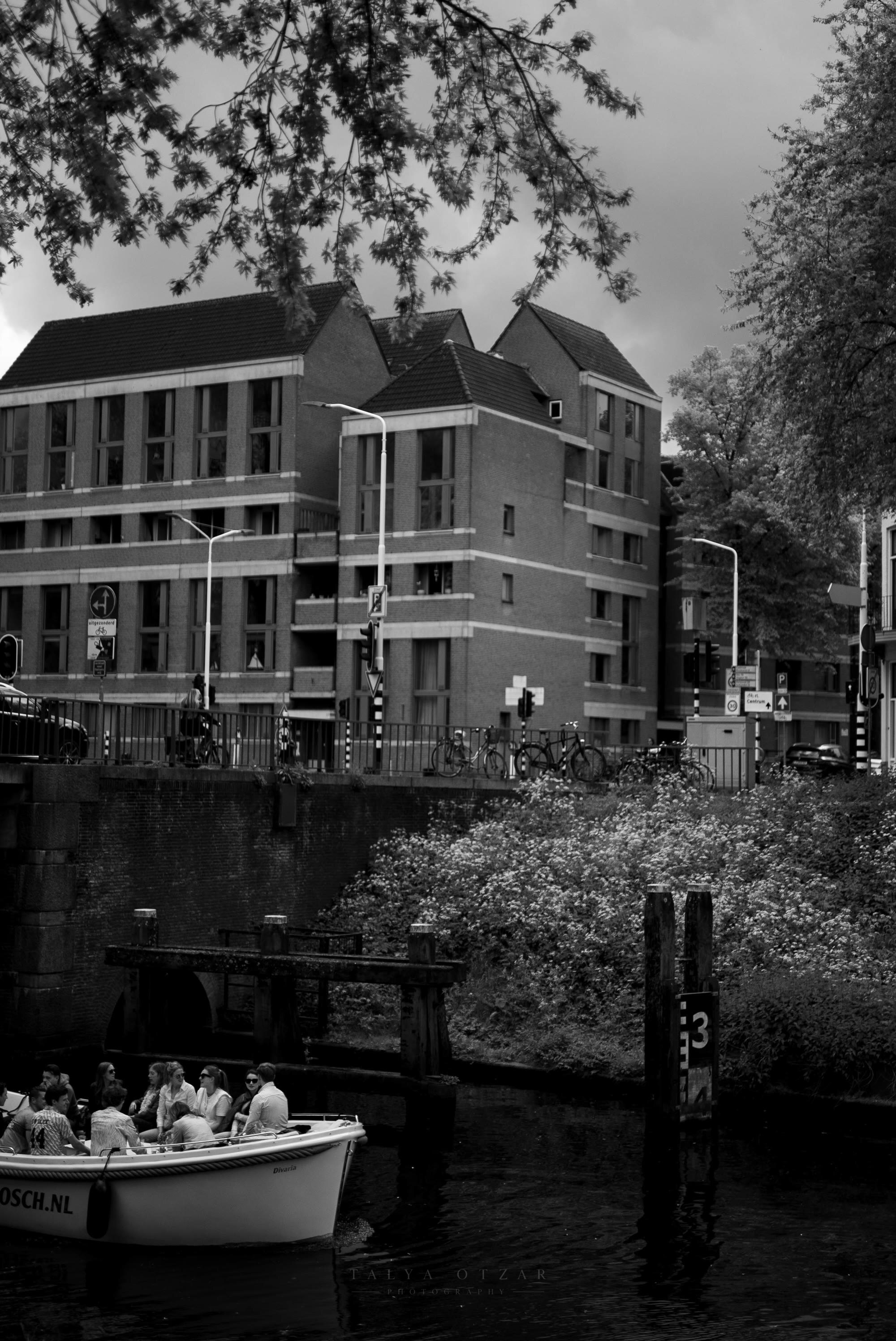 A tour boat of passengers passing beneath the brick buildings on the canal