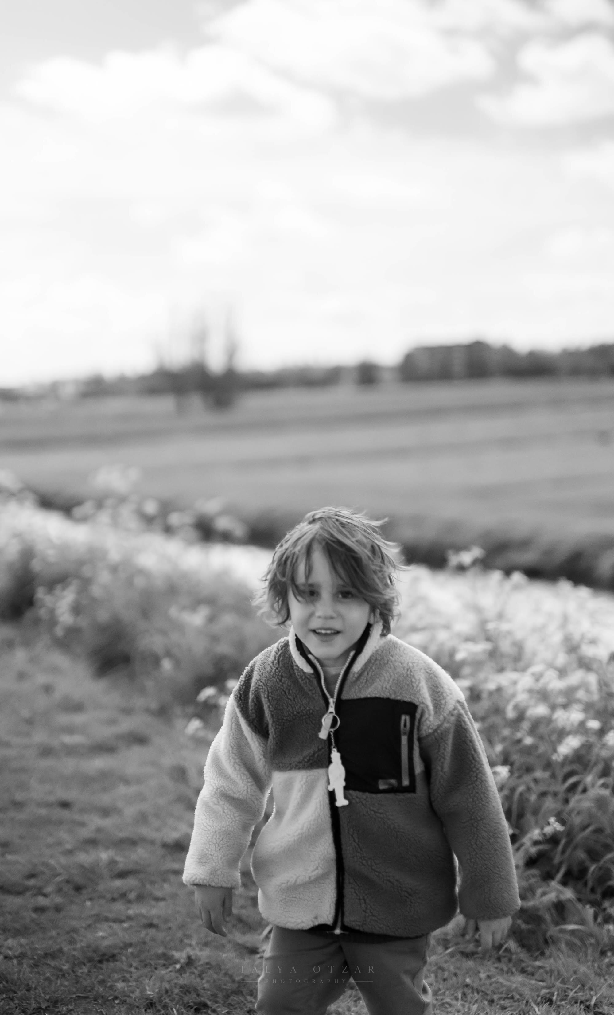 A child in a fleece standing on a field path, flat farmland stretching behind