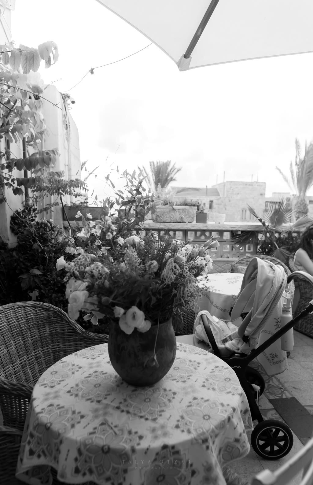 A jug of flowers on a lace-covered table on a Jaffa terrace, a pram parked beside it