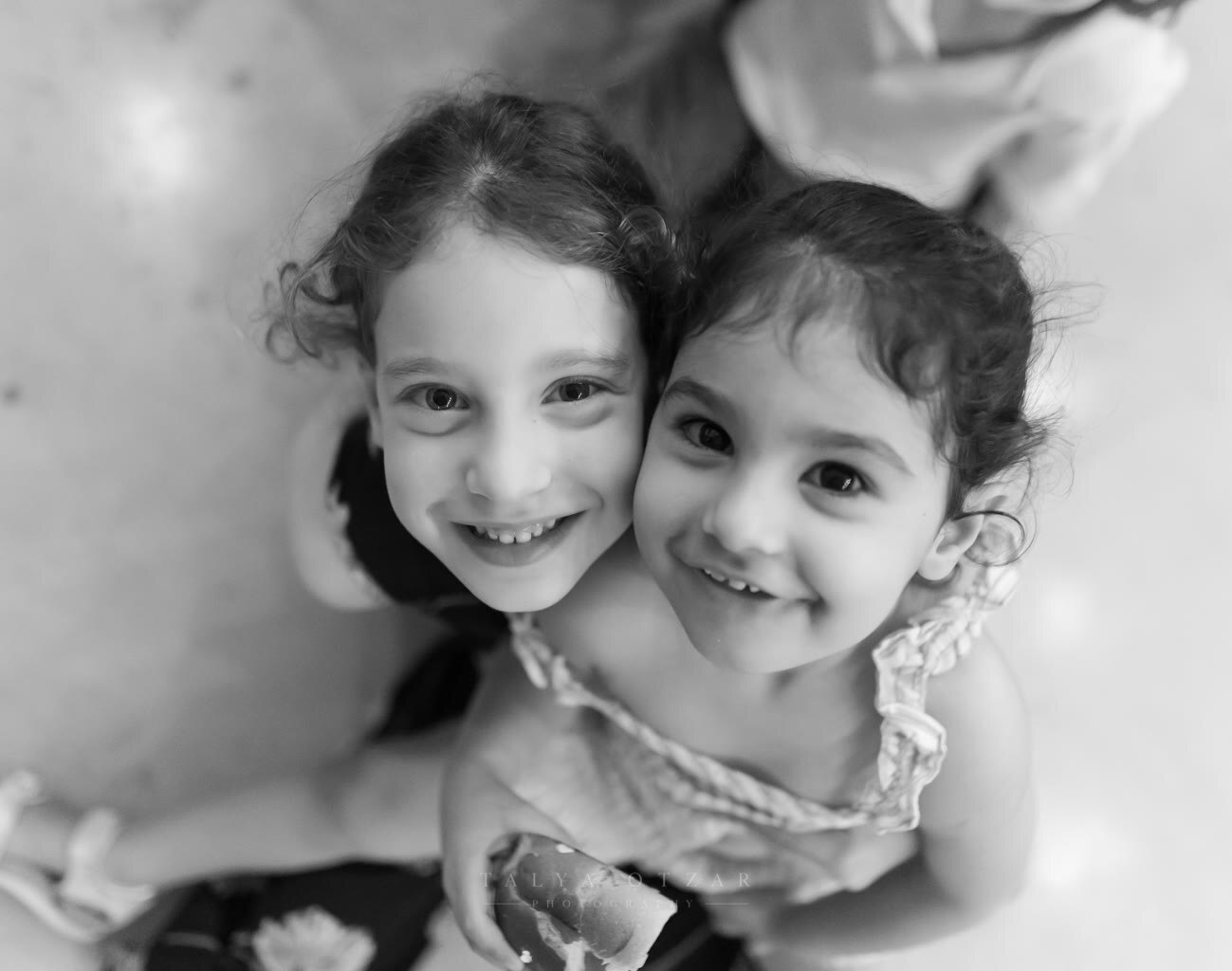 Two sisters cheek to cheek, smiling up at the camera
