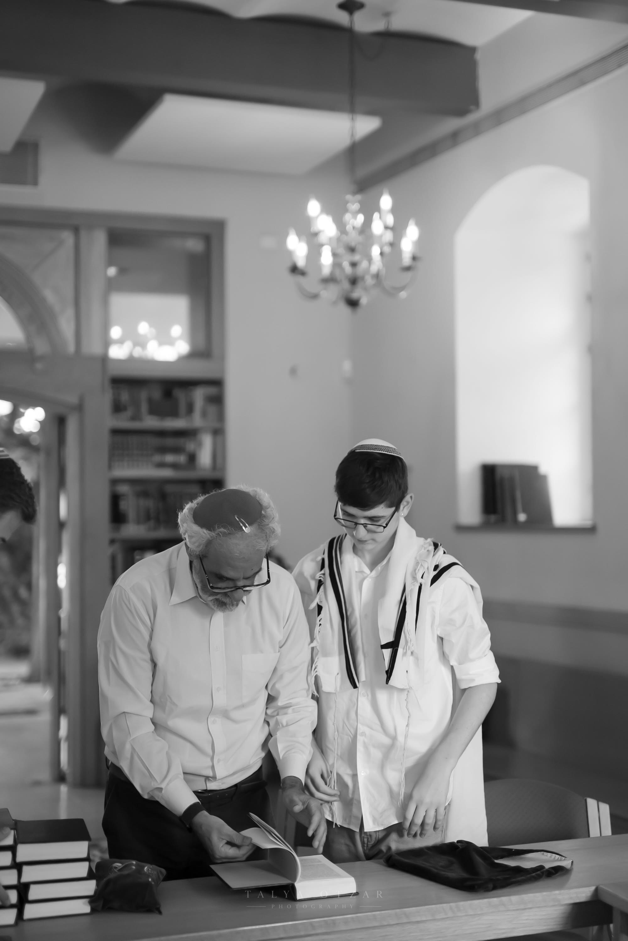 A grandfather and his grandson in a tallit going through the reading together before the bar mitzvah