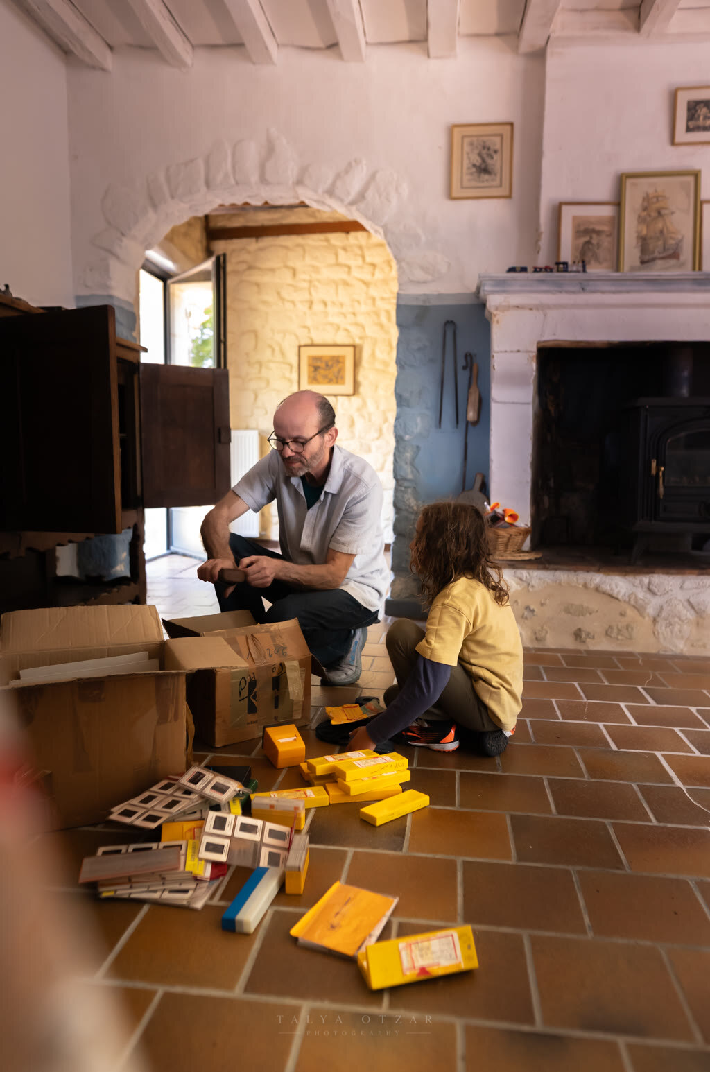 Father and child sorting boxes of old slides on the tiled floor of the farmhouse