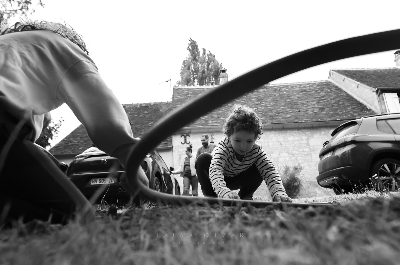 A child playing with a hose on the grass outside the stone house, photographed low