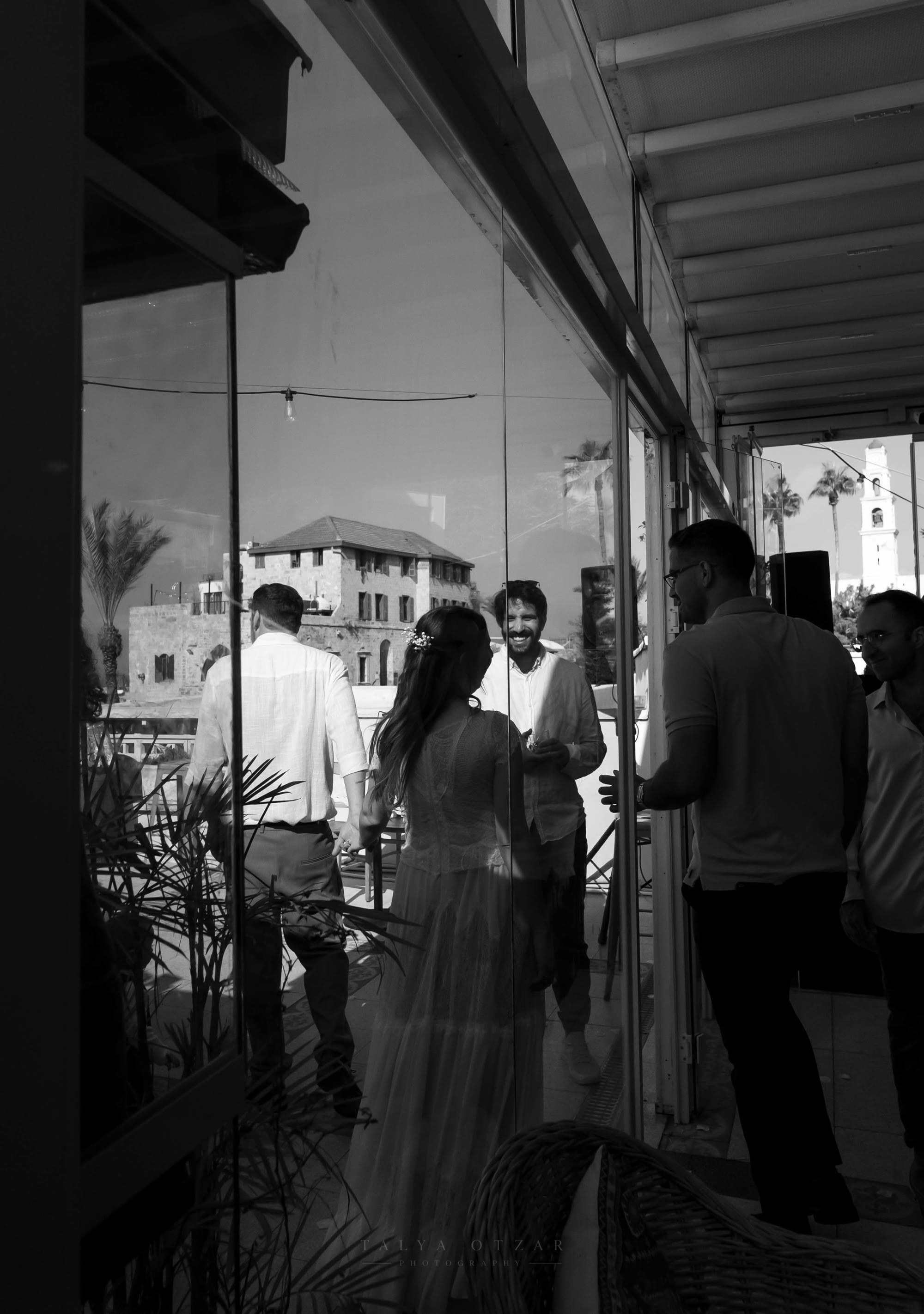 Guests reflected in the glass of a Jaffa venue, a girl in a tulle dress among them