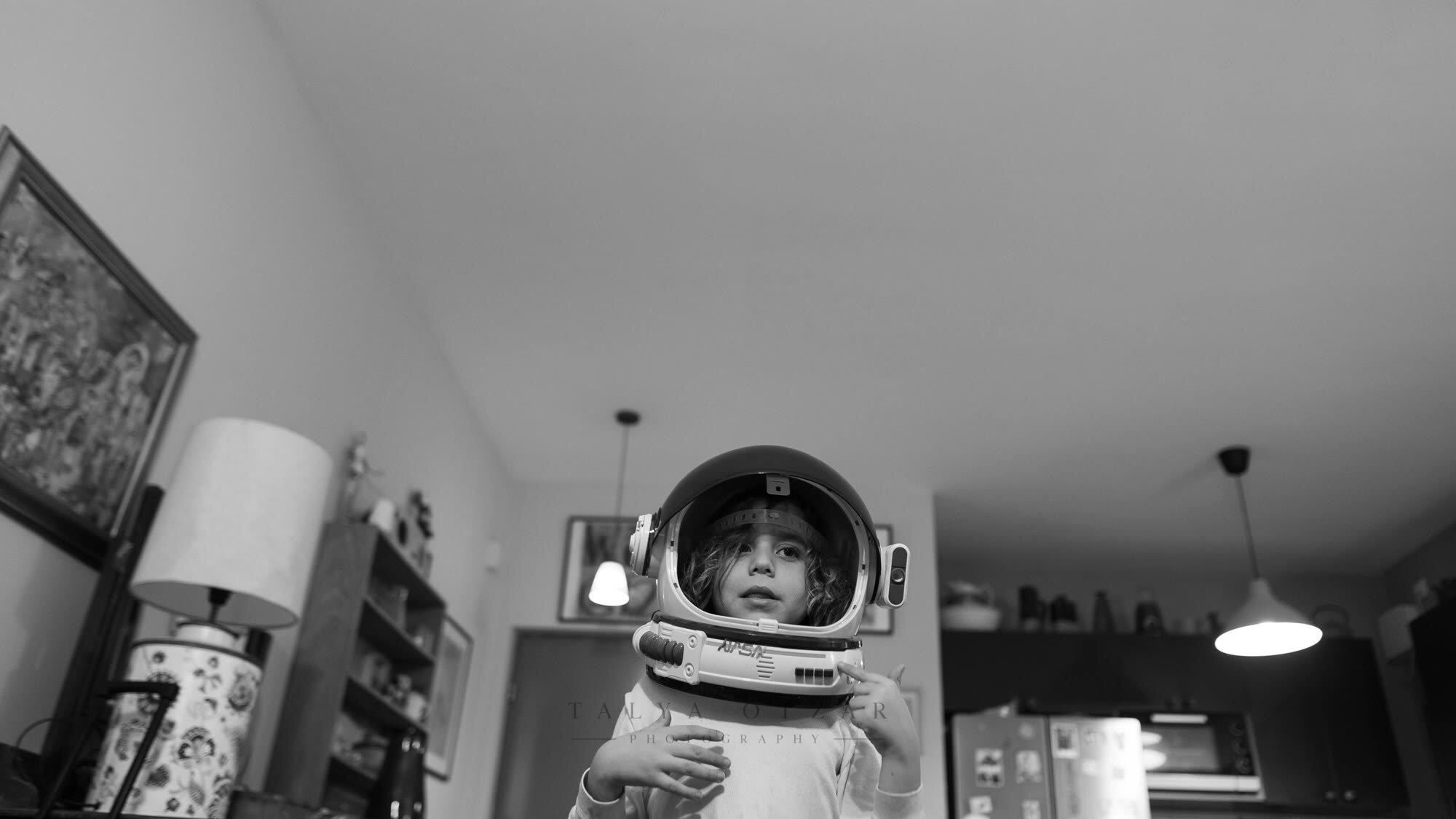 A child standing in the living room in a toy astronaut helmet