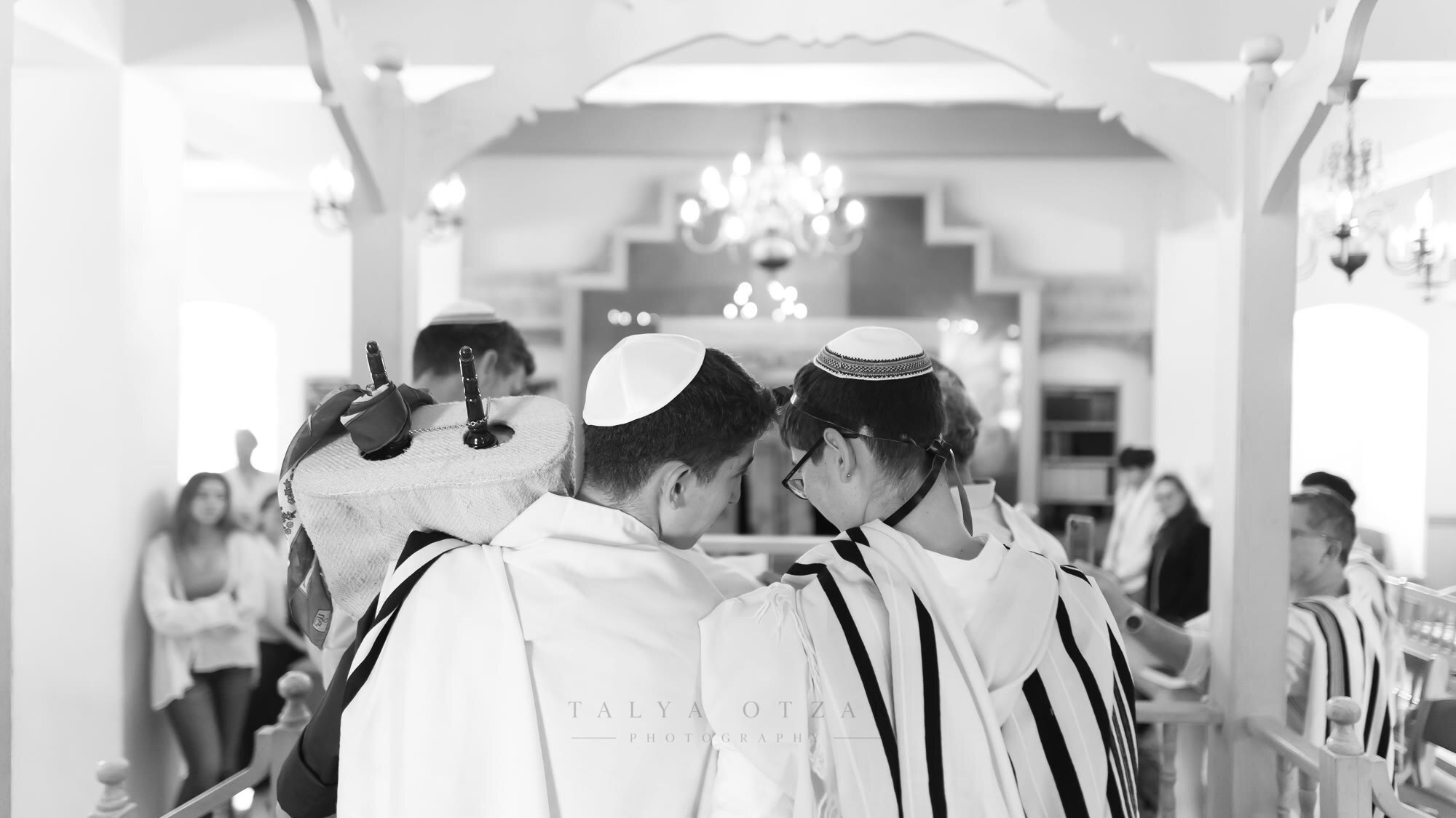 Two boys in prayer shawls side by side as the Torah scroll is carried past