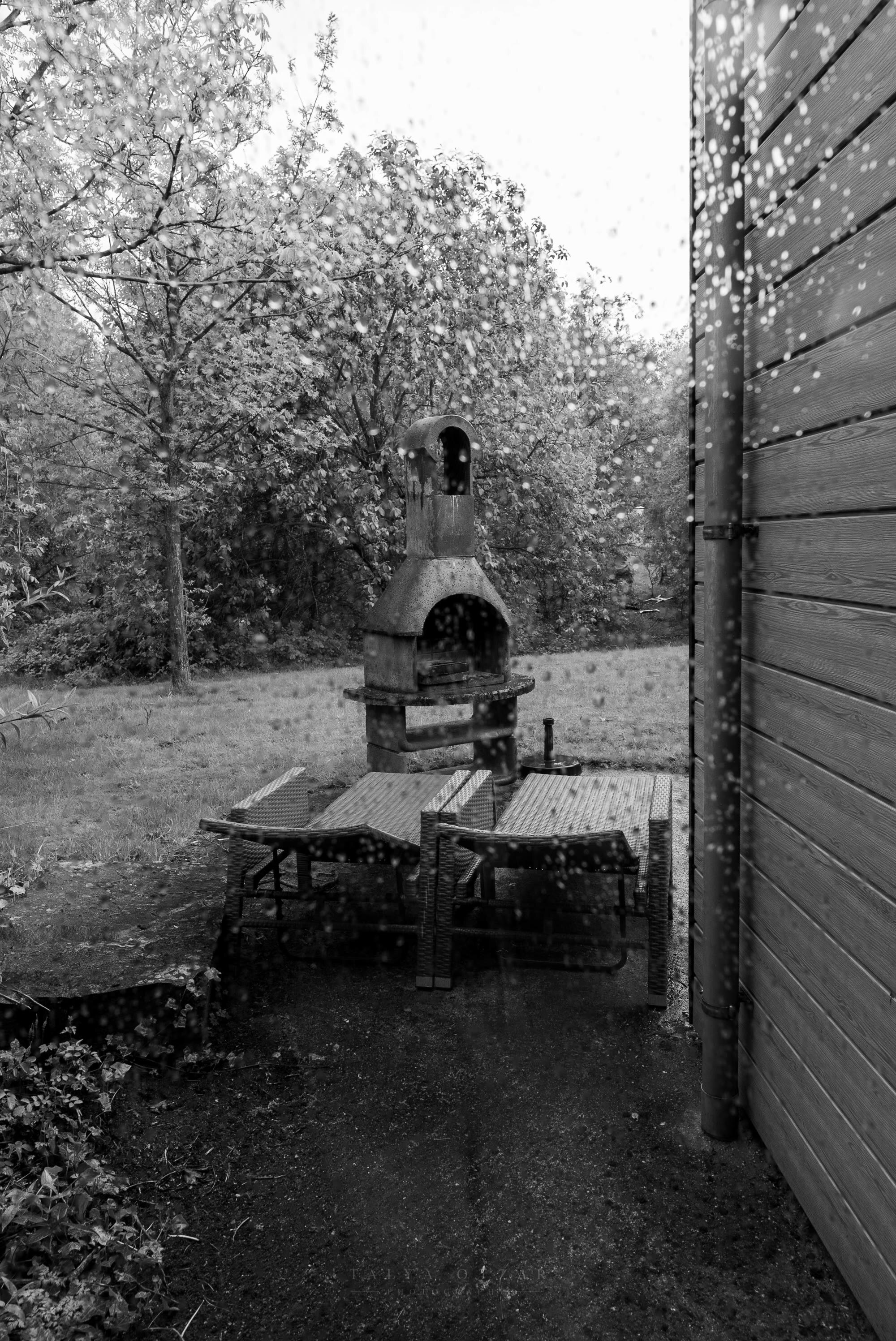 The garden barbecue and benches seen through a rain-flecked window