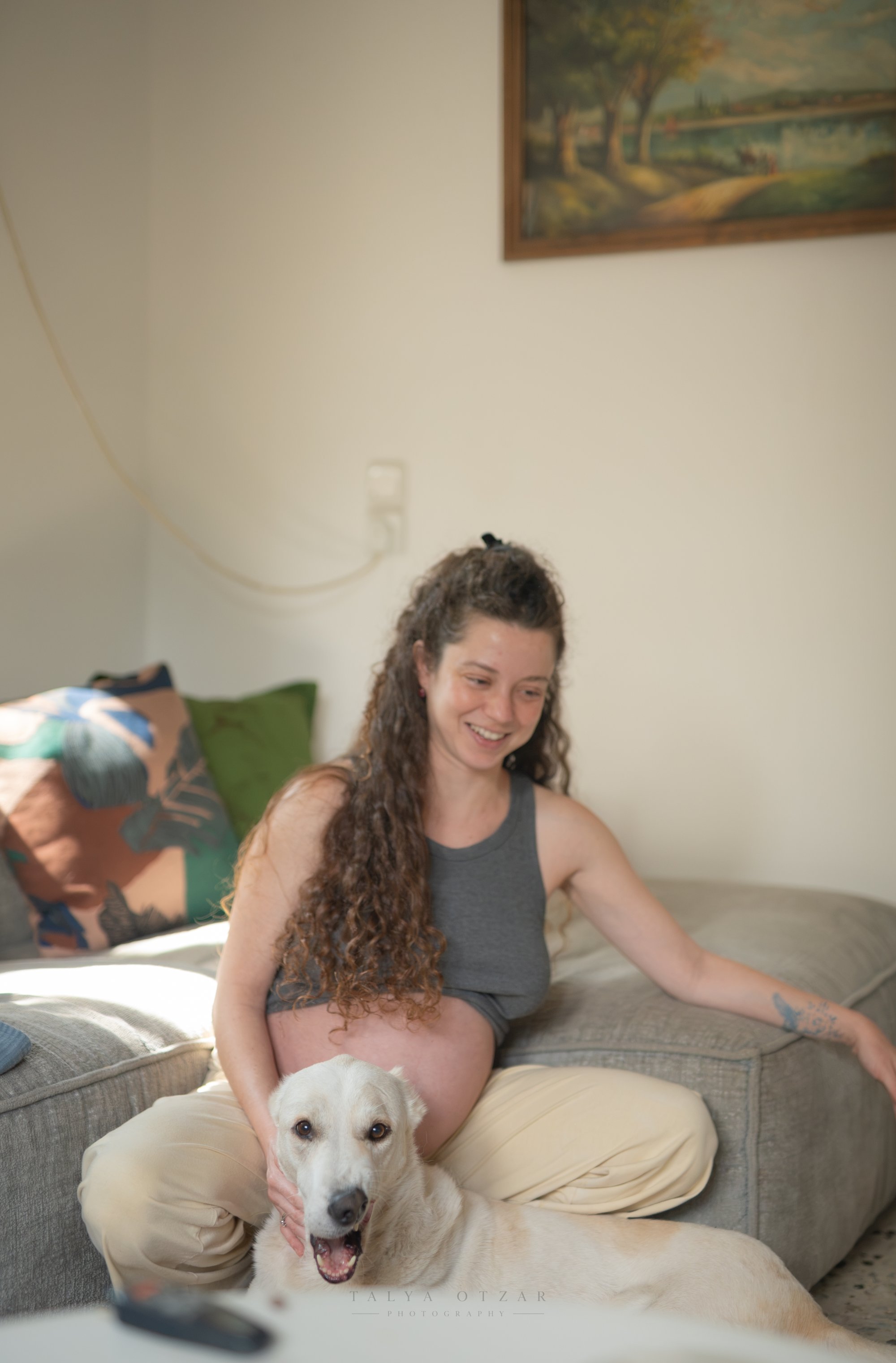 הכלב הלבן מניח את ראשו על ברכיה של סיגי, ממש מתחת לבטן