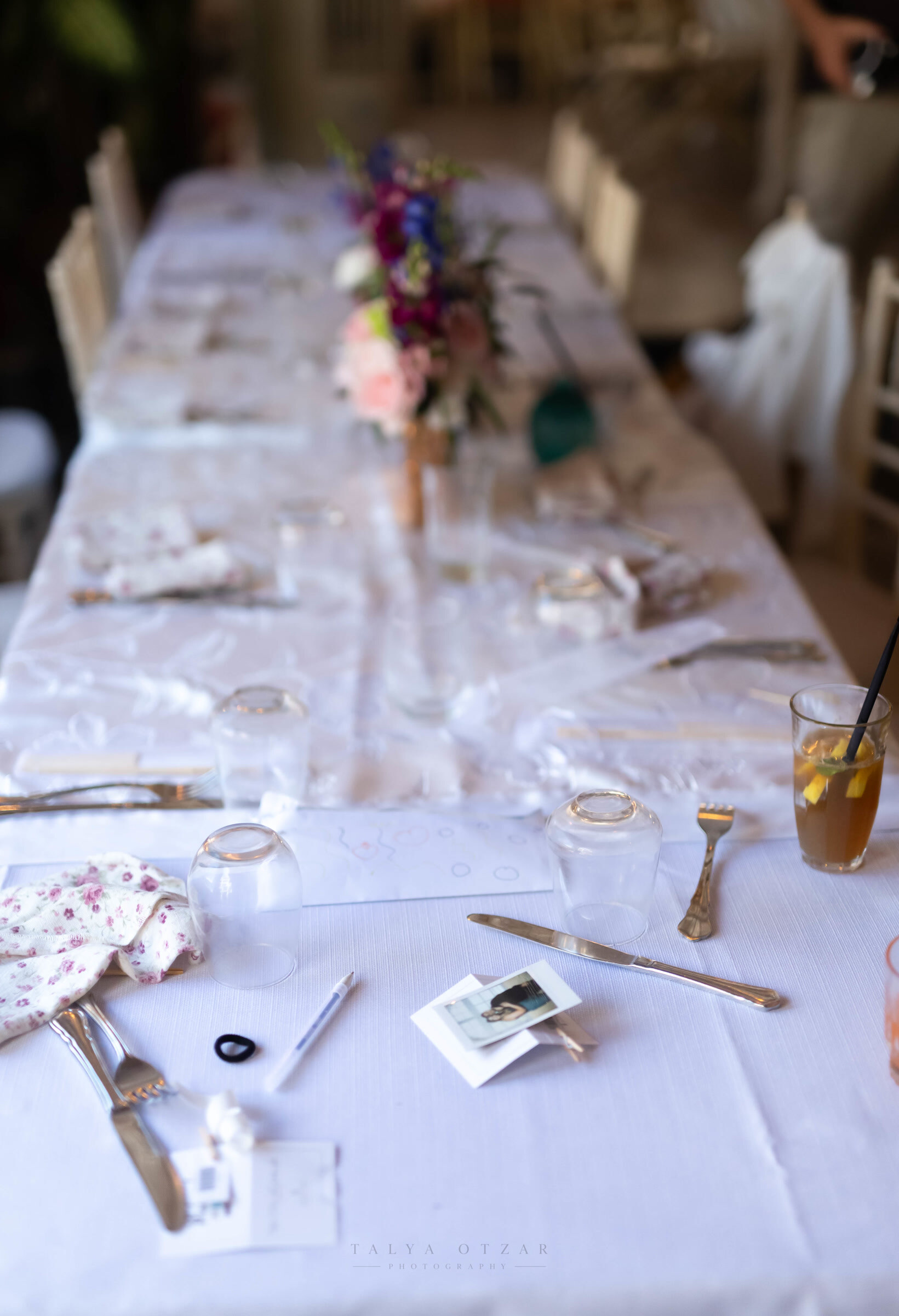 The long banquet table after the meal — upturned glasses, the cake knife and an instant photograph left on the cloth