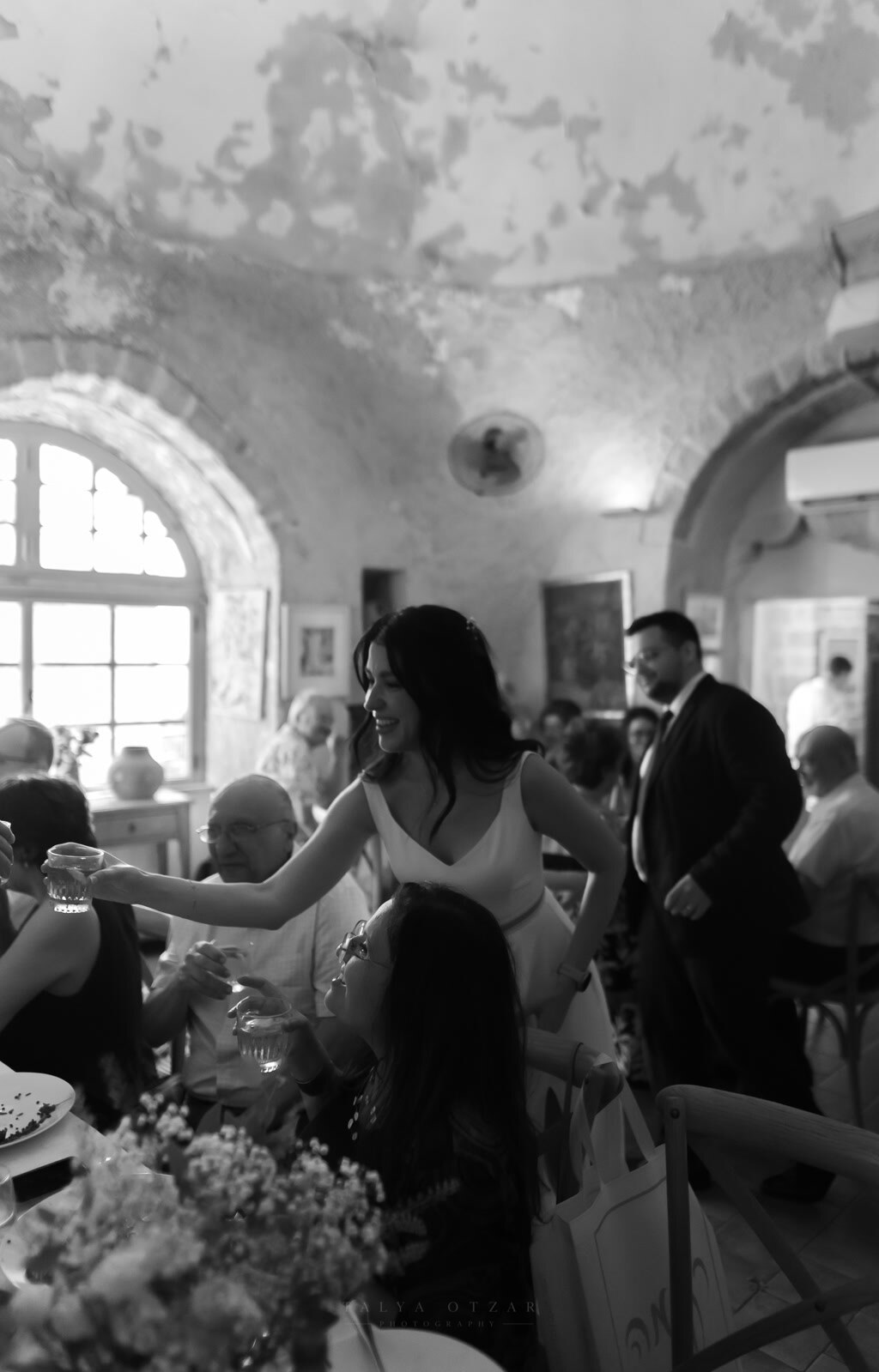 The bride leans across the table to raise a glass with a guest in the vaulted stone hall