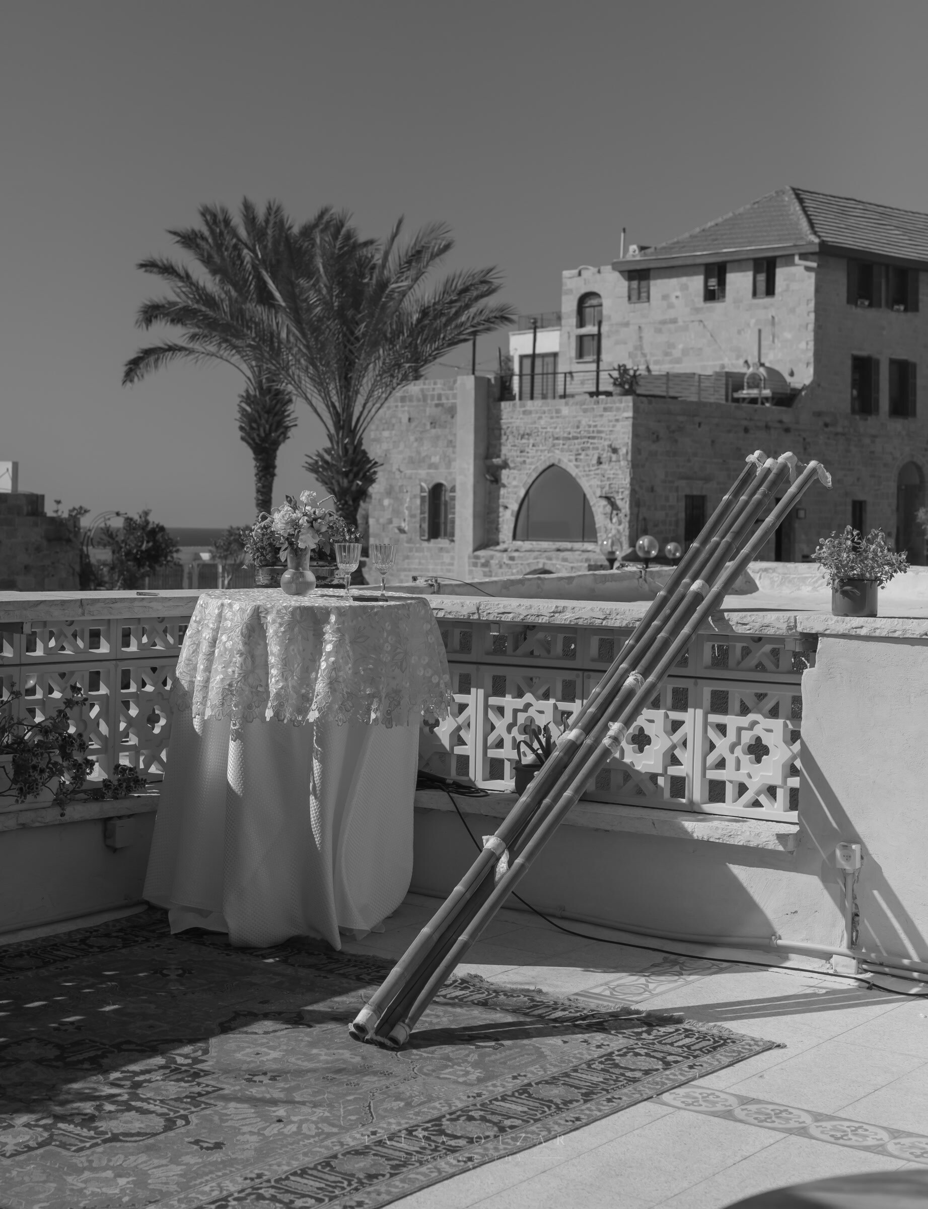 The chuppah poles waiting against the balustrade of a Jaffa rooftop, the sea on the horizon