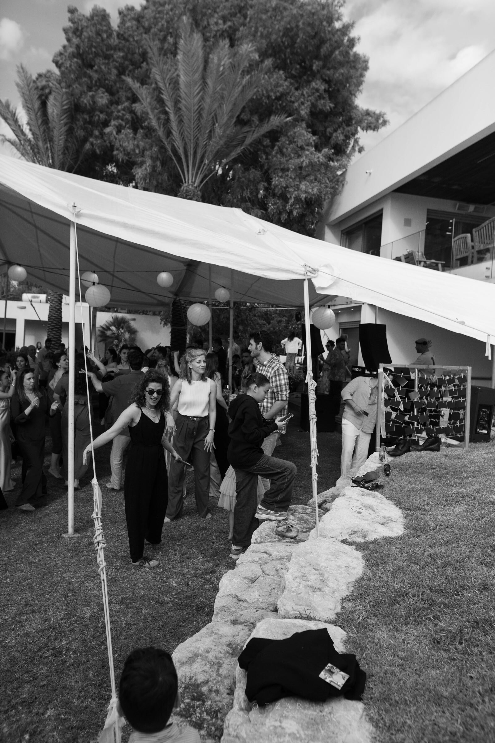 Guests dancing on the grass beside the marquee, paper lanterns and palm trees above them