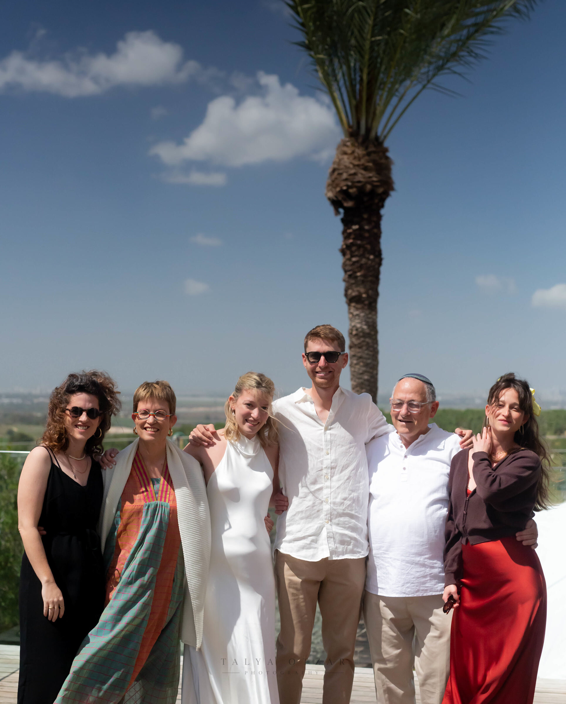 Bride, groom and family lined up for a portrait on the terrace, a palm tree and open fields behind