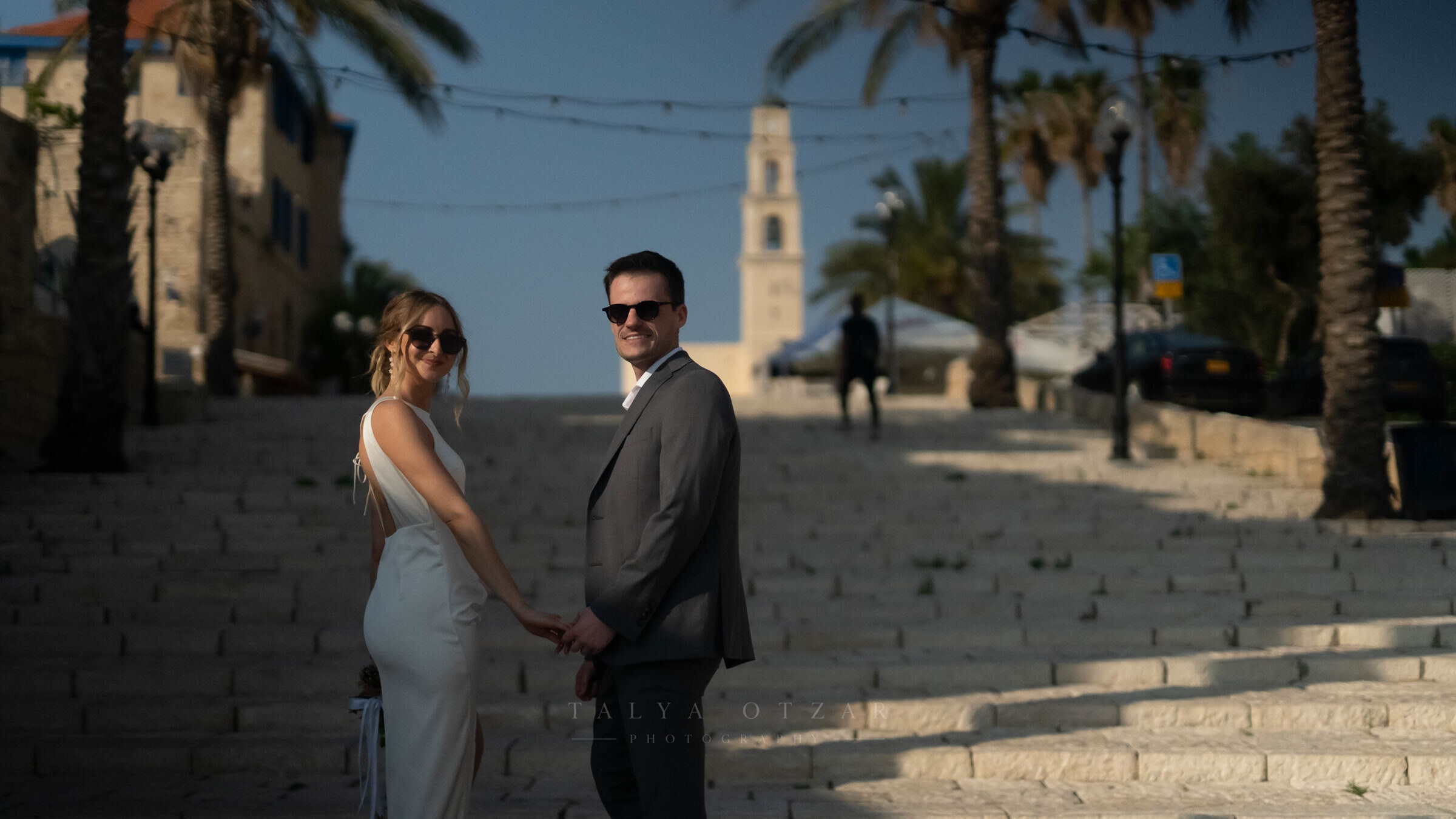 The couple pausing hand in hand on the Jaffa steps in low evening sun