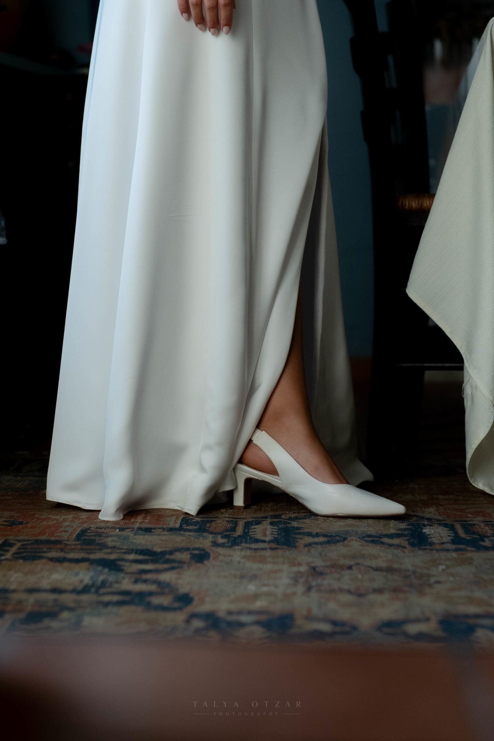 The bride's white heel and the hem of her satin dress against an old patterned rug