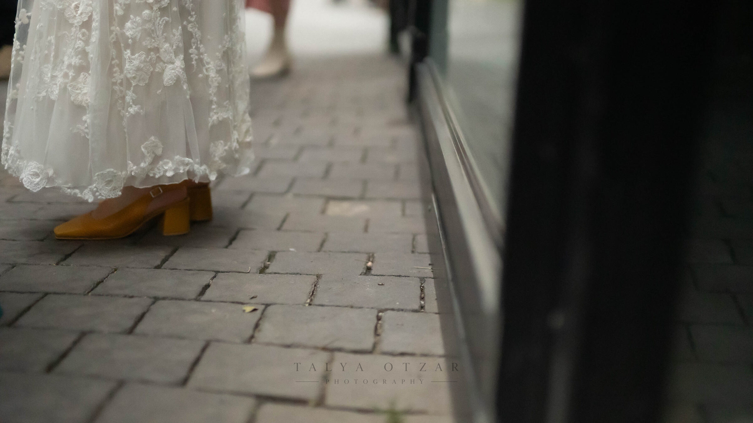 Mustard-yellow heels beneath a lace hem as the bride walks along a paved street