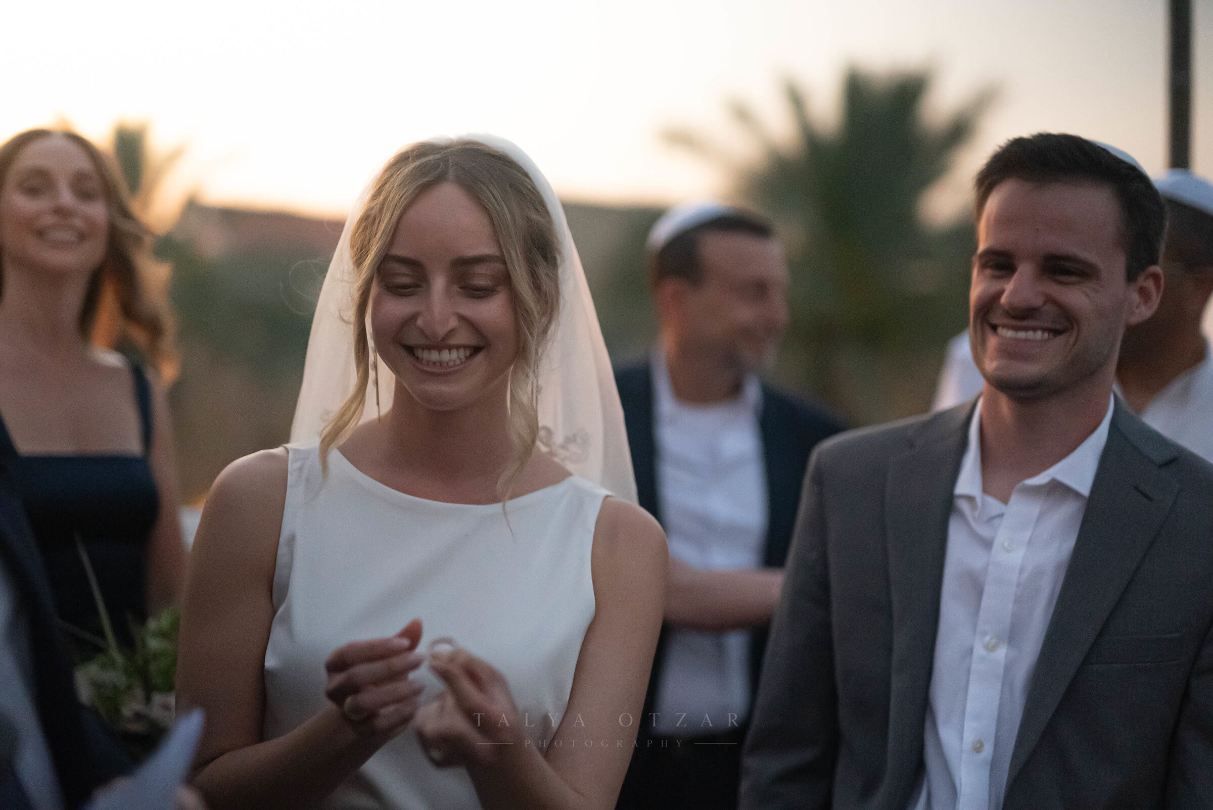 The bride smiling with the ring in her hand, the groom beside her at dusk