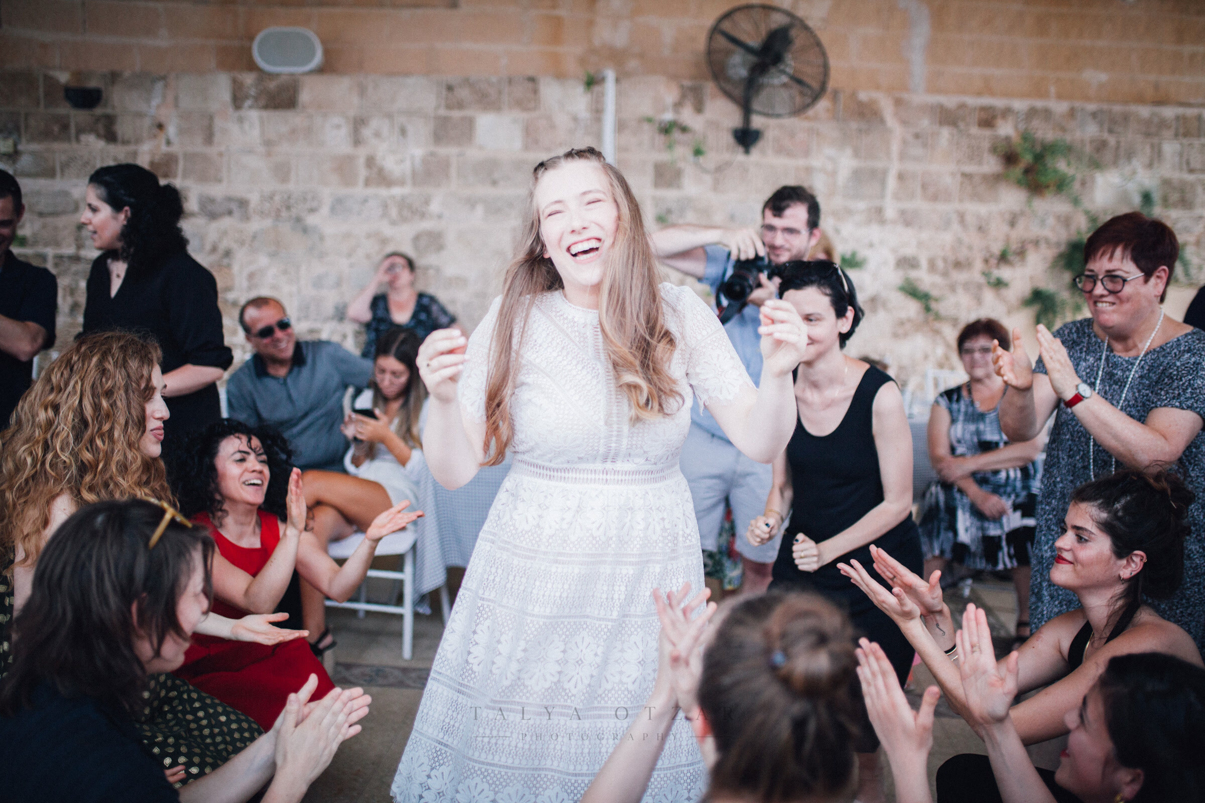 A guest laughing in the middle of a circle of clapping friends in the stone hall