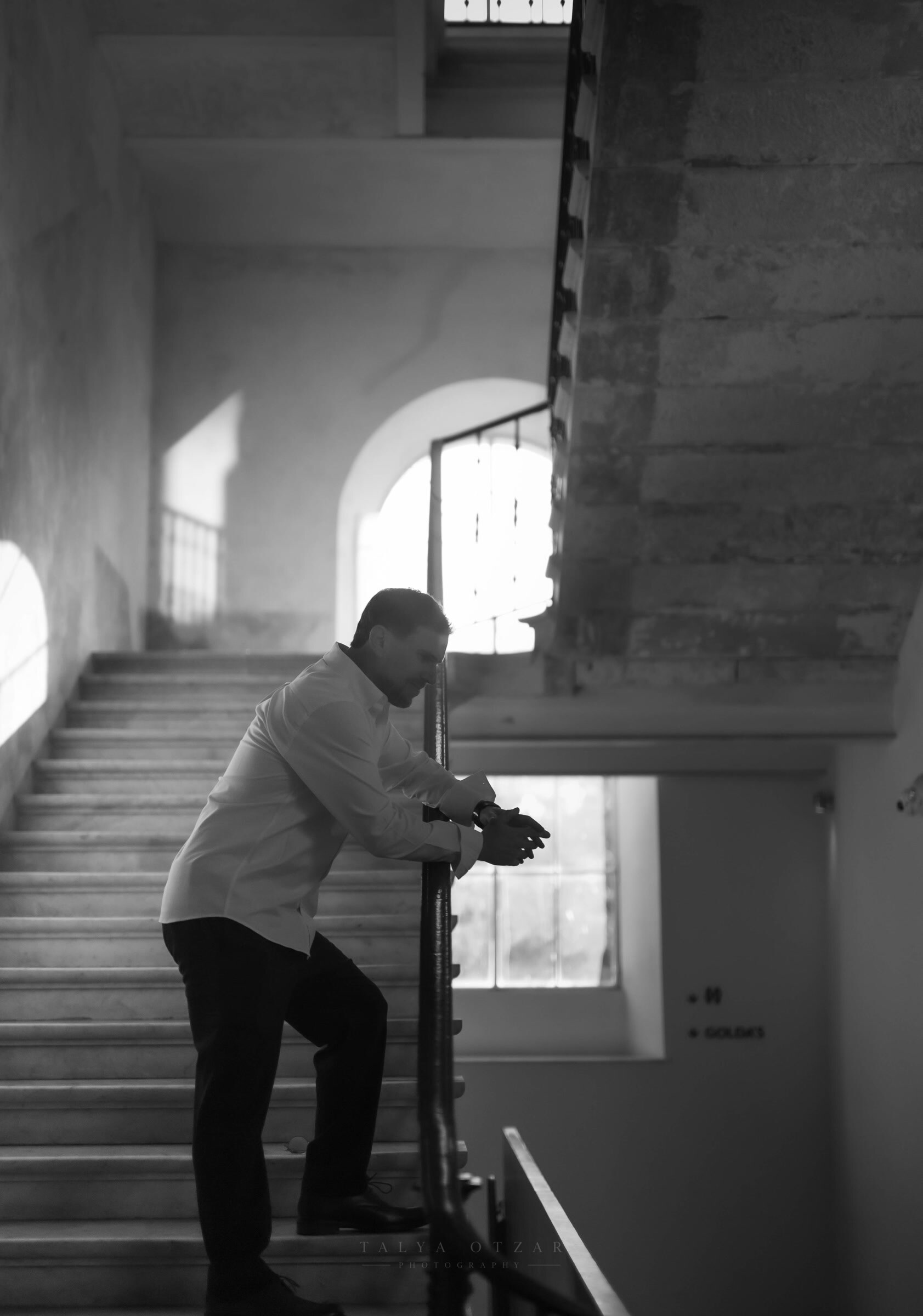 A guest leaning on the banister of the old stairwell, light from the arched window behind