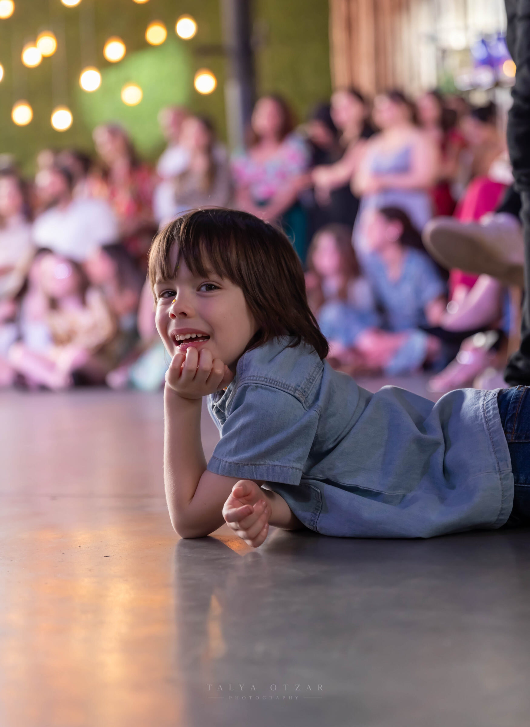 A small child lying on the dance floor, chin on hands, watching the party