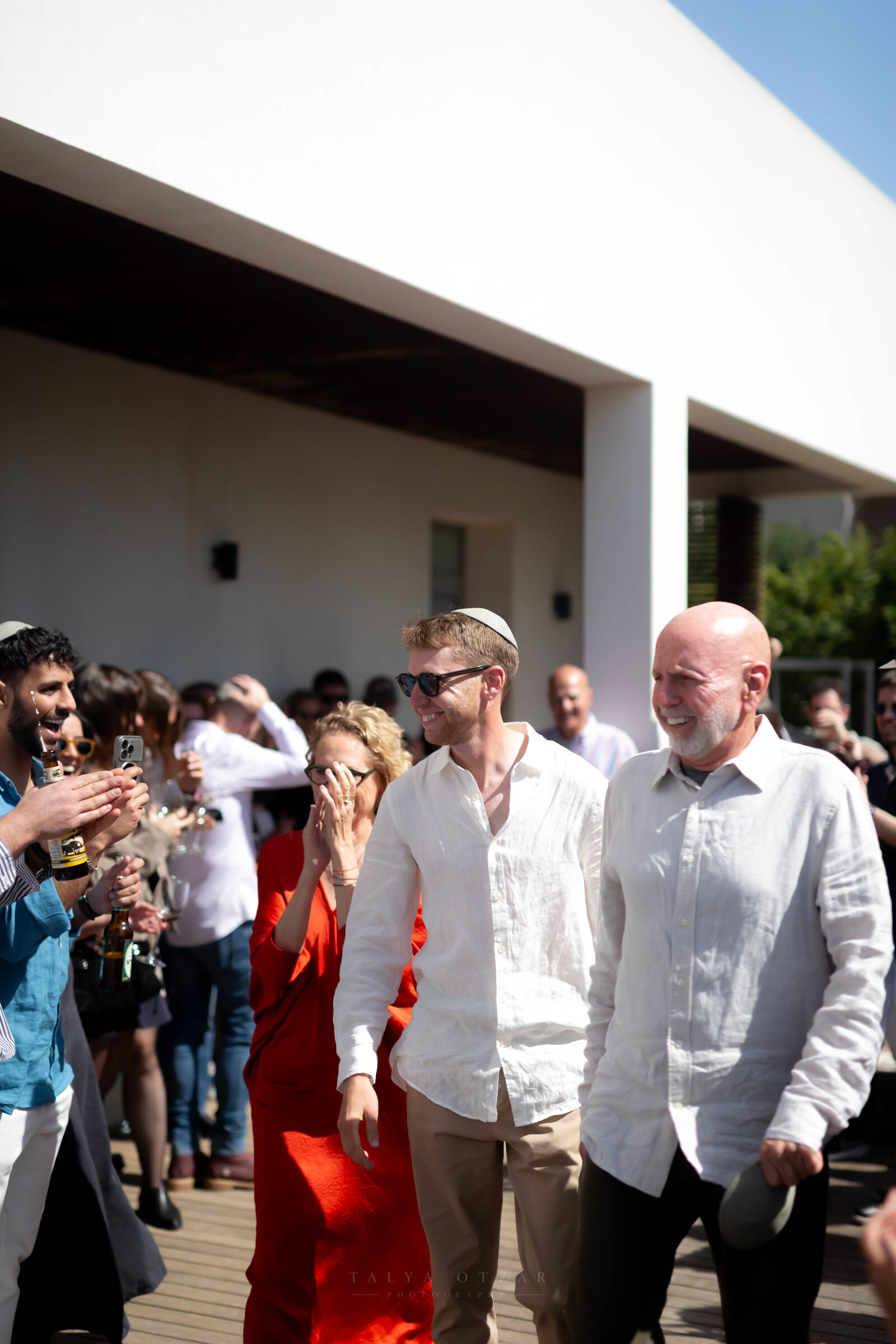 The groom walking in with his father as guests raise their glasses and film