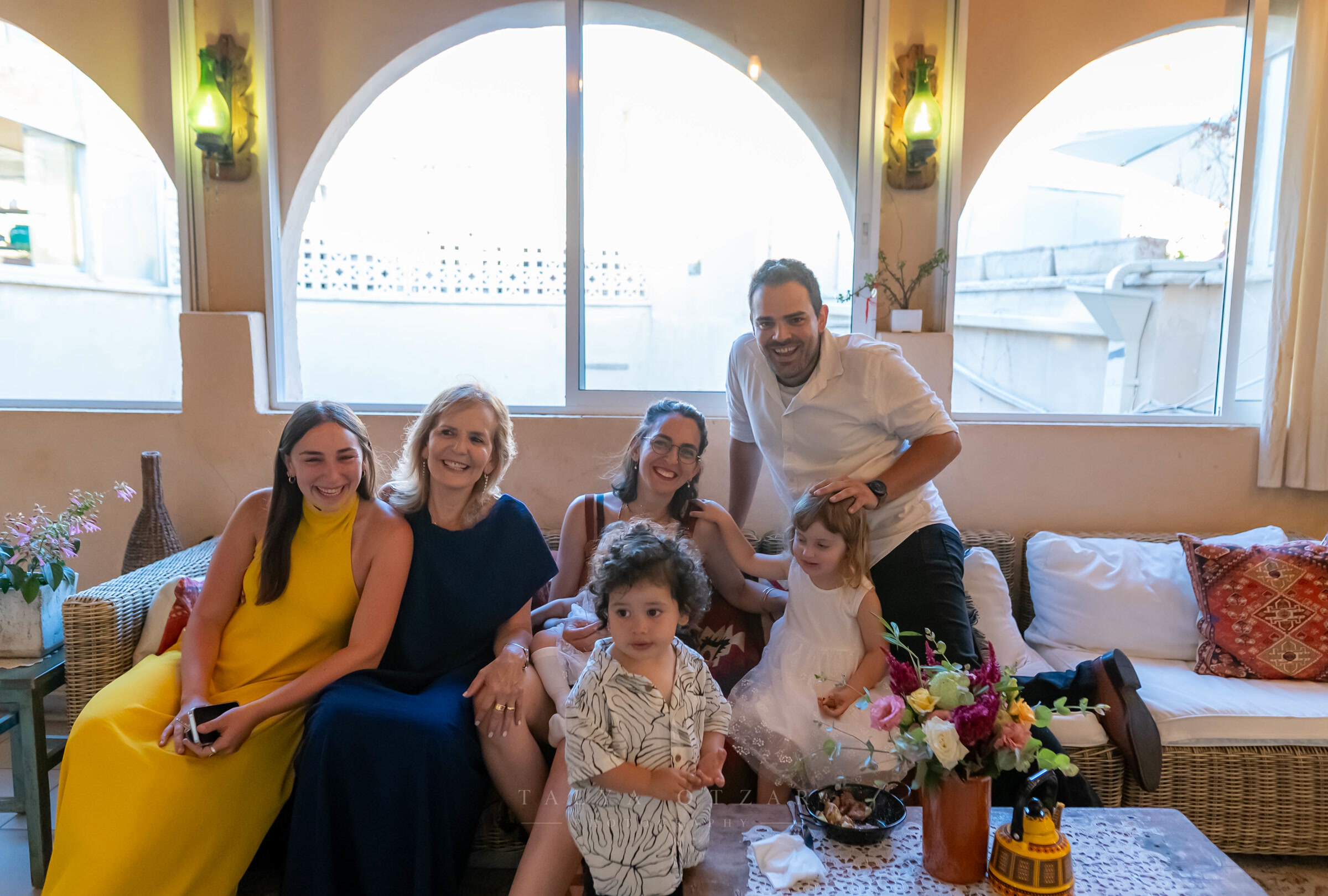 Family sitting together on the sofa in a room of arched windows, the youngest two in front