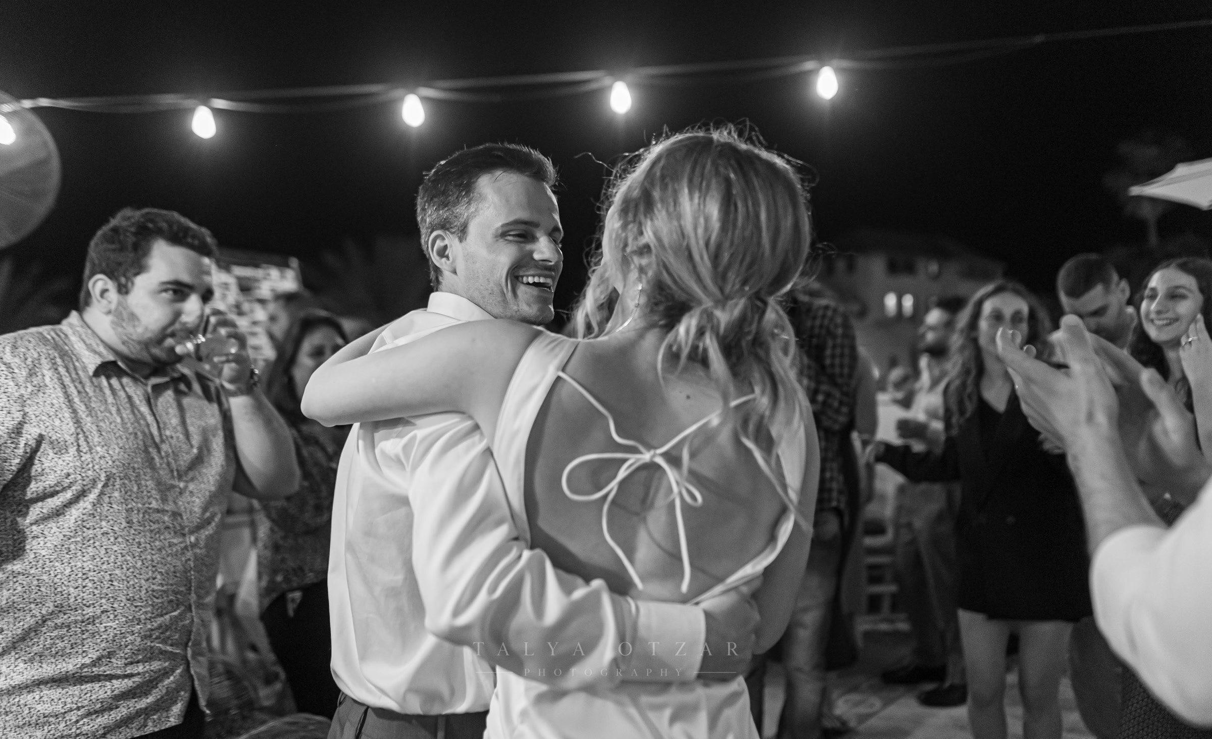 The couple holding each other on the dance floor at night, guests clapping around them