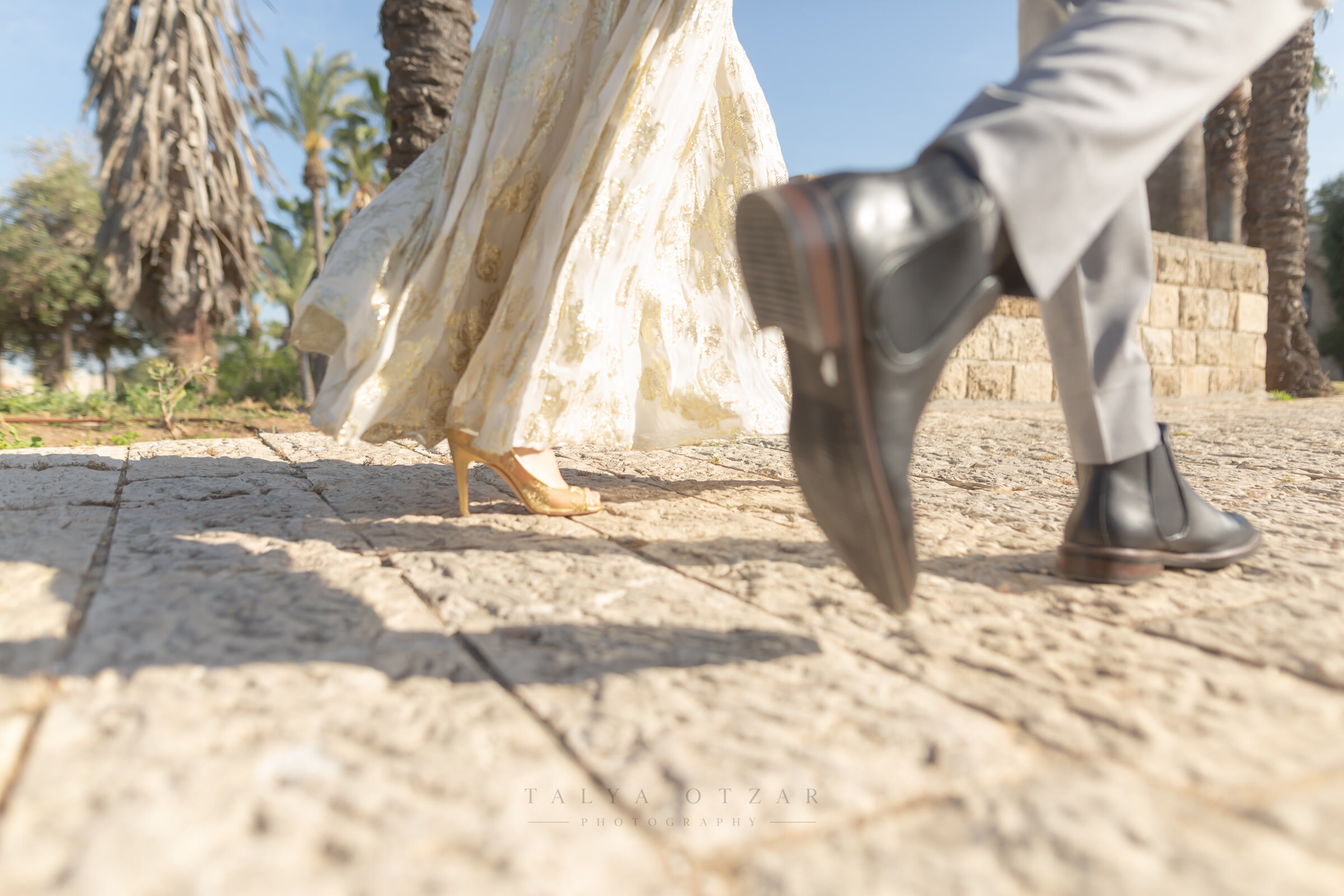 Bride's and groom's feet mid-step on the stone paving, palms rising behind