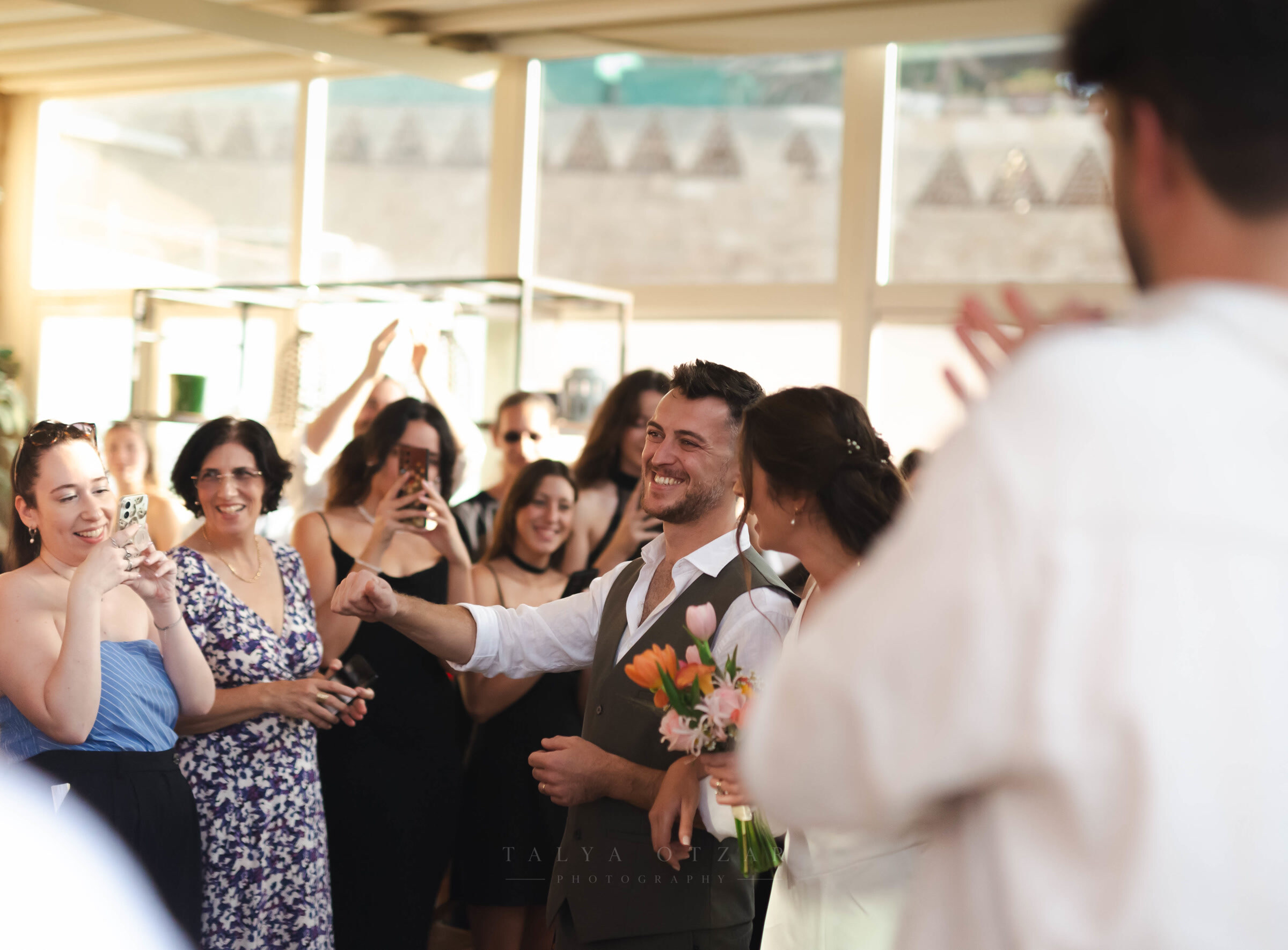 The groom laughing as the couple are surrounded by clapping guests at the seaside venue