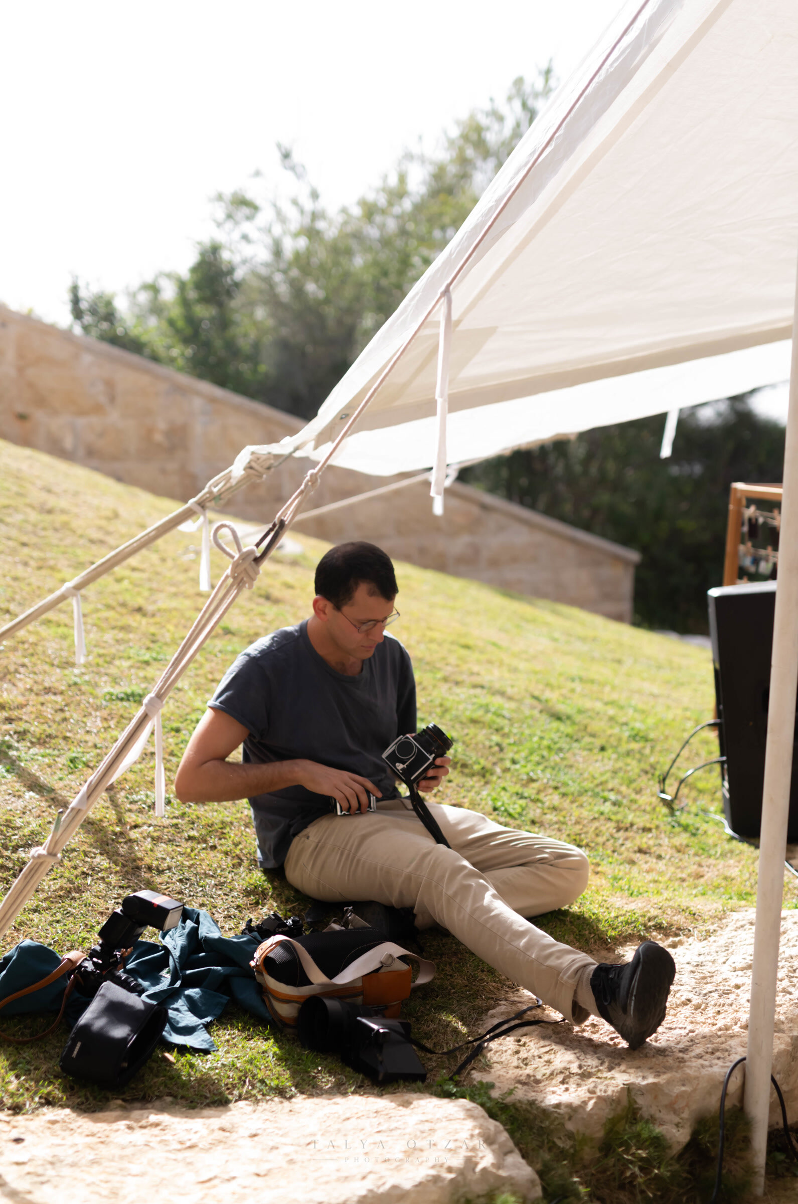 A guest sitting on the grass at the edge of the marquee, loading a medium-format film camera