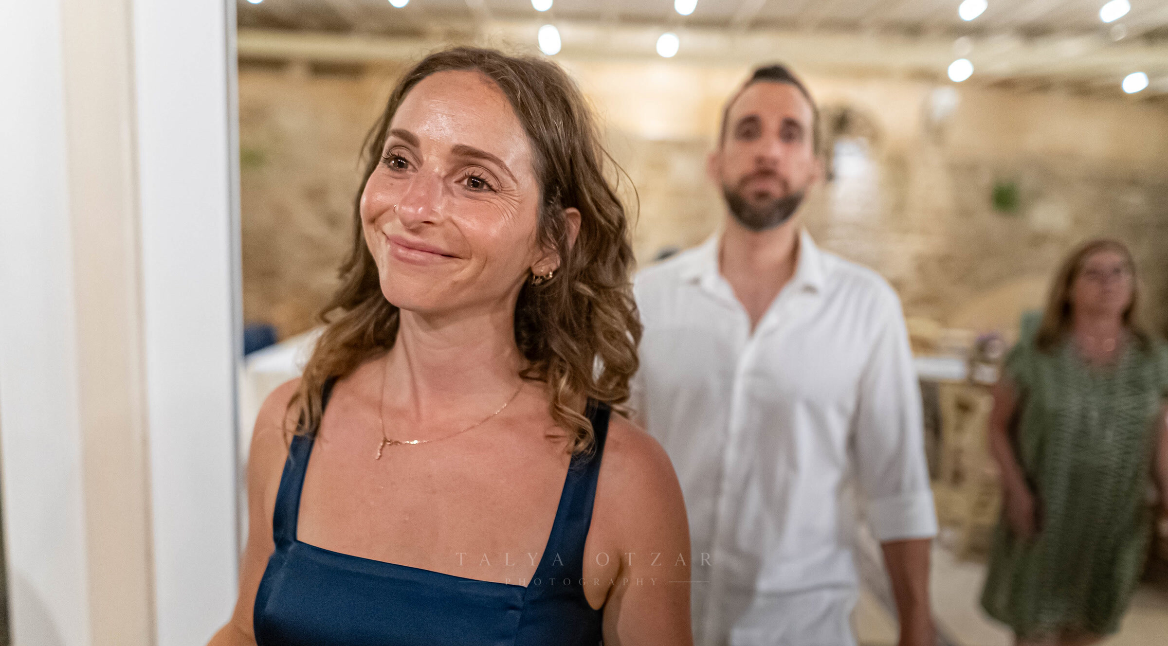 A guest smiling in the stone-walled venue, festoon lights strung above