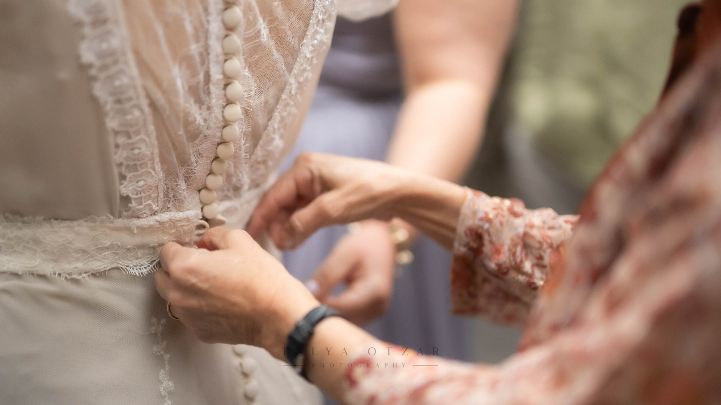 Hands doing up the row of tiny buttons at the back of the lace wedding dress