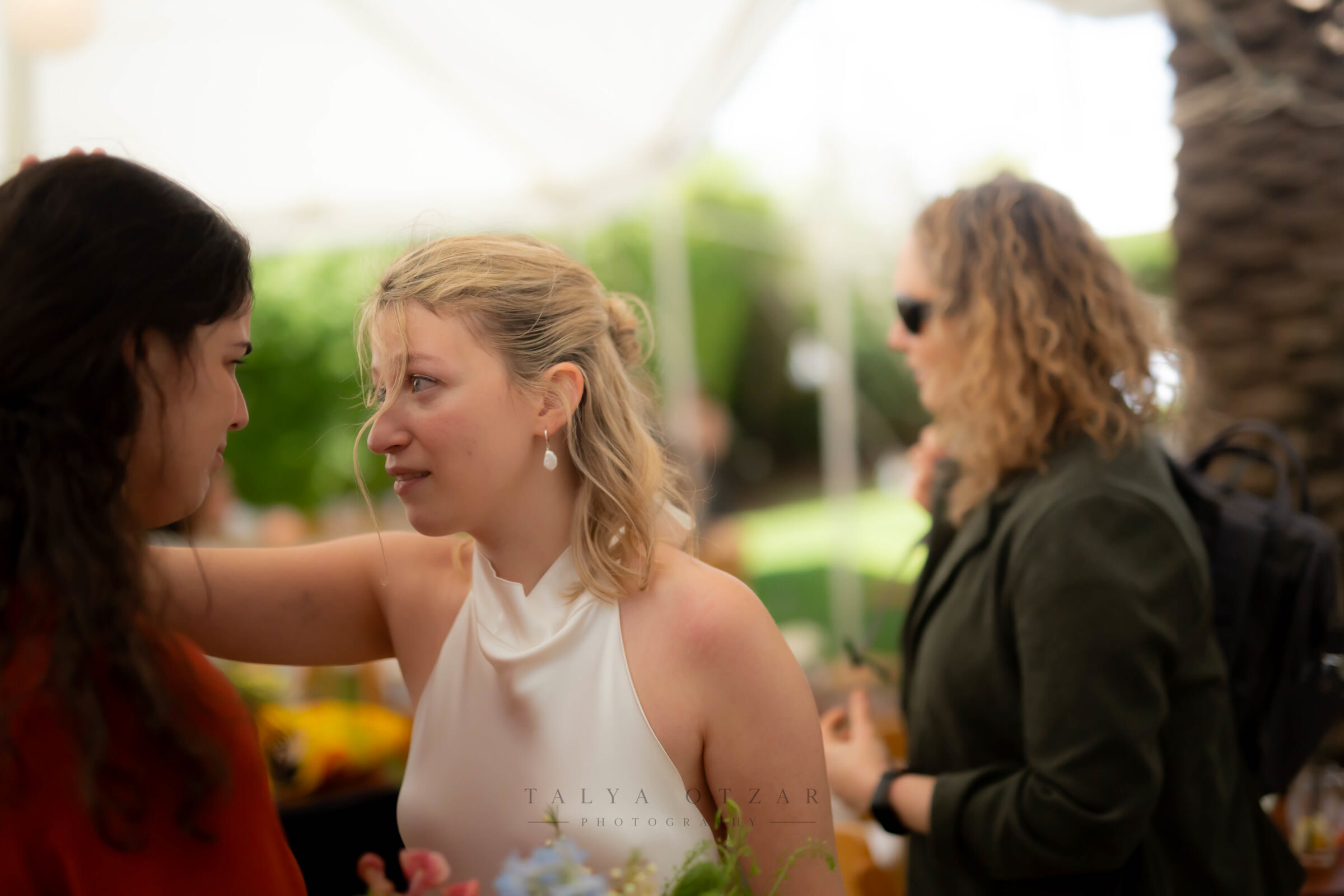 The bride listening with wet eyes as a friend rests a hand on her shoulder