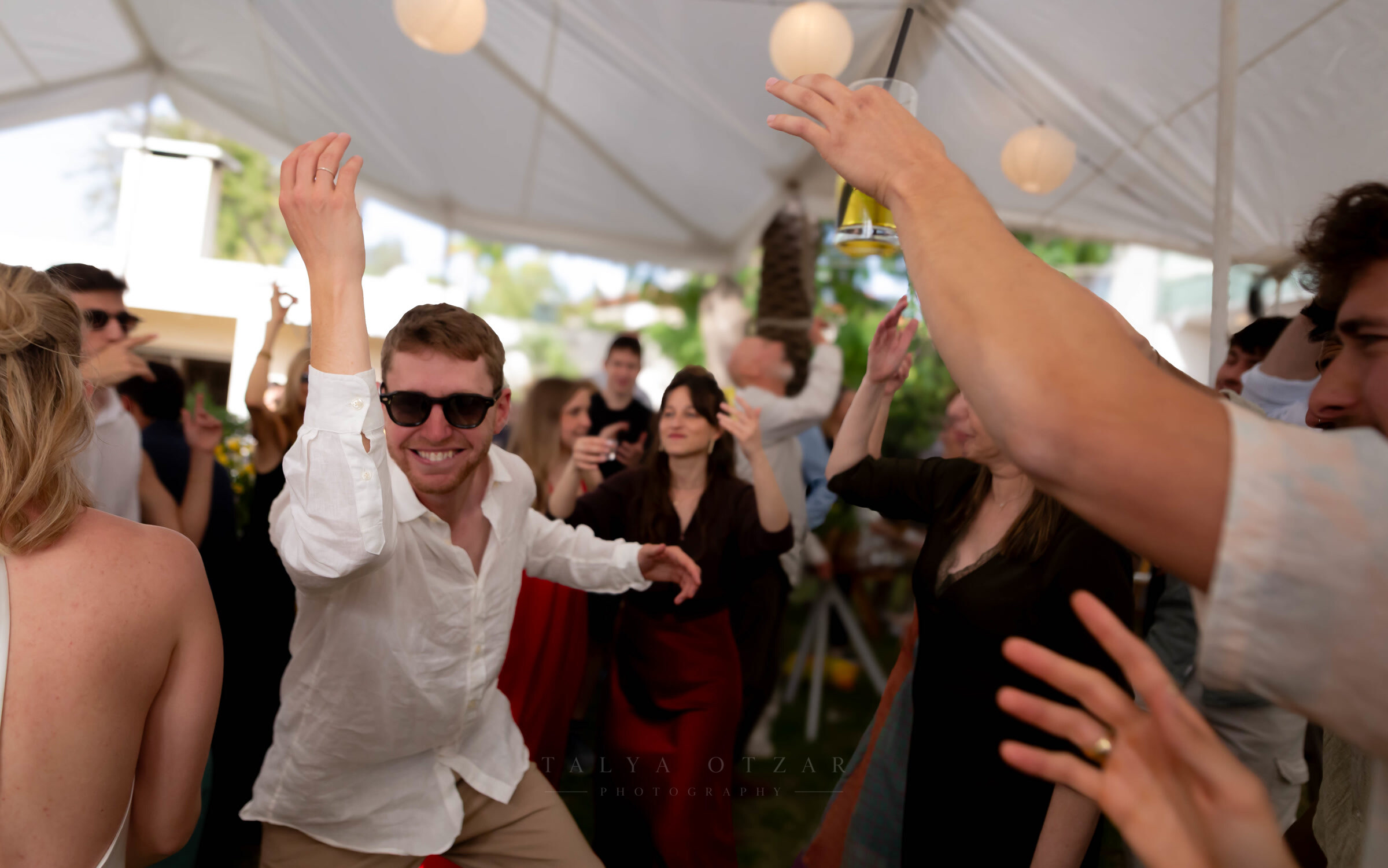 A guest dancing with both arms up beneath the marquee's paper lanterns