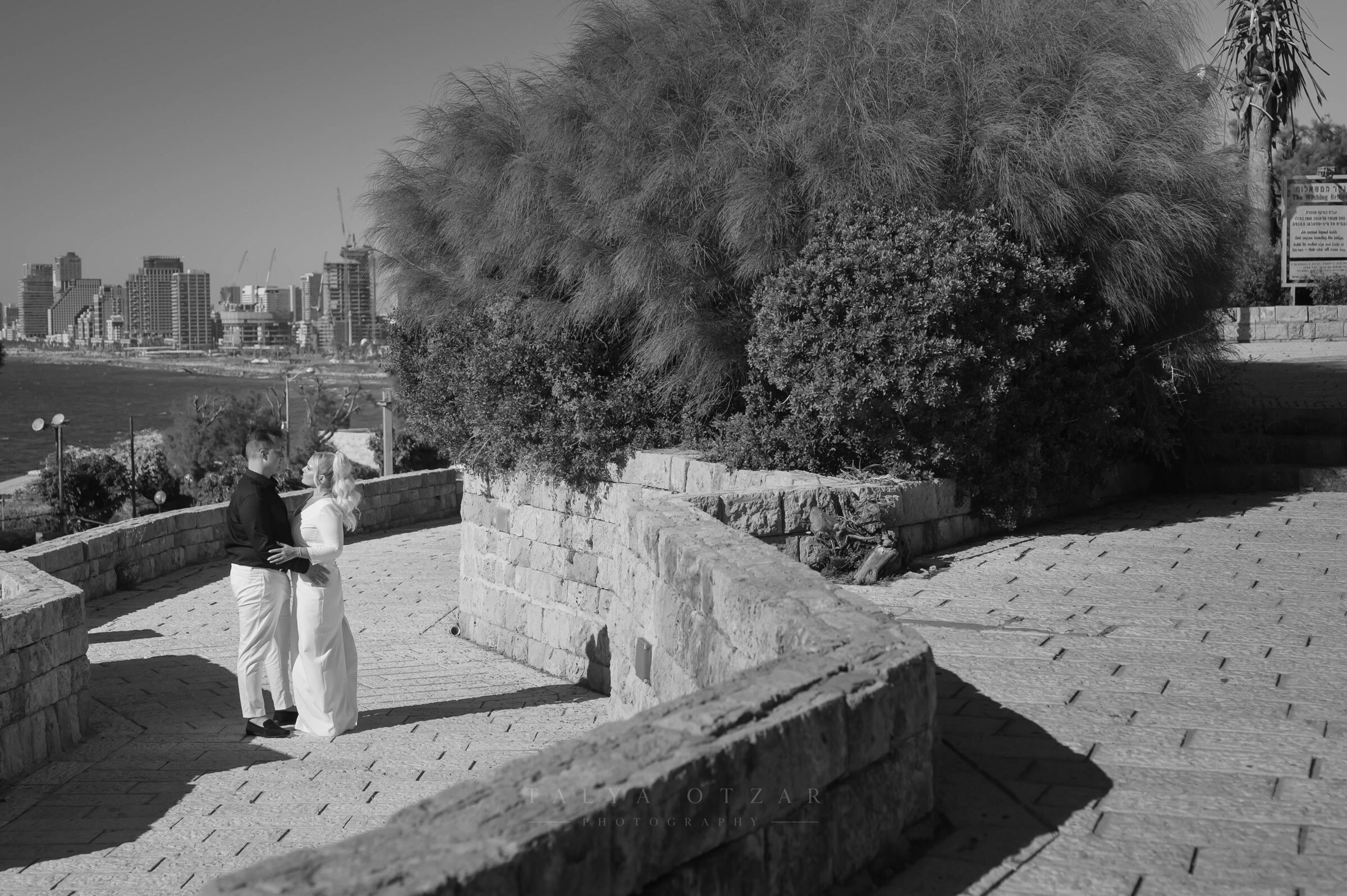 The couple standing together on the Jaffa promenade with the Tel Aviv skyline across the bay
